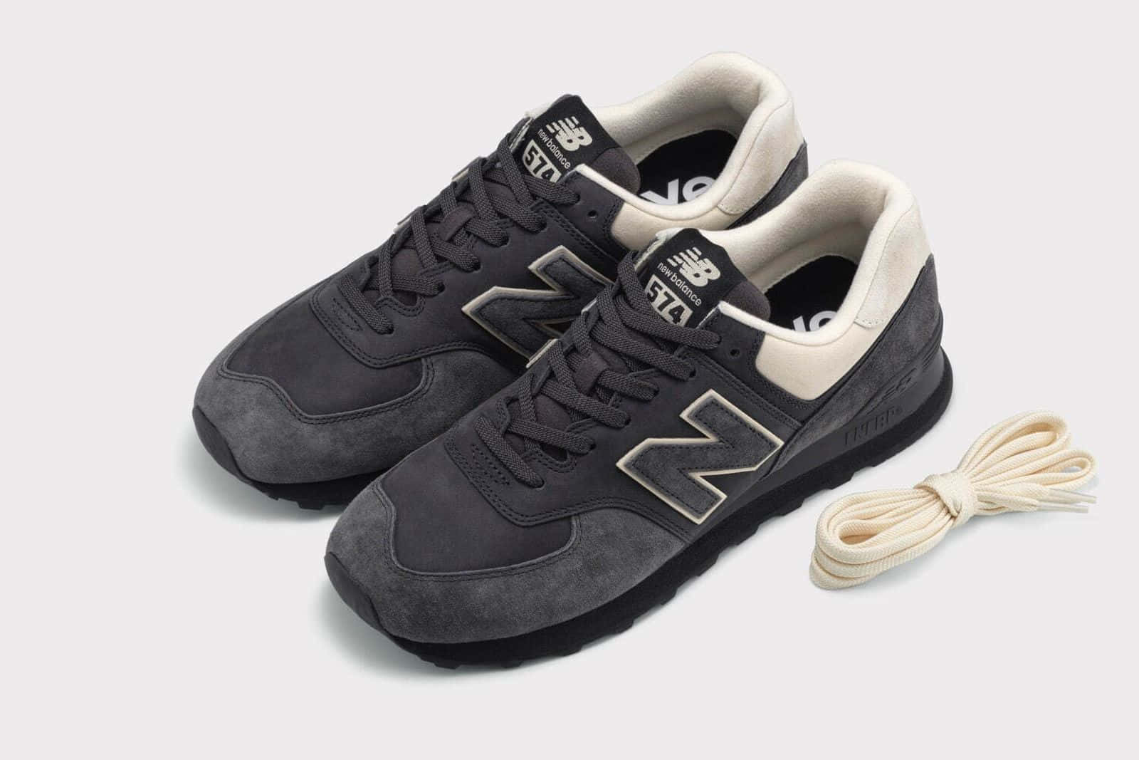 深灰色麂皮 New Balance 574 運動鞋，帶有奶油色點綴和鞋帶，白色背景。