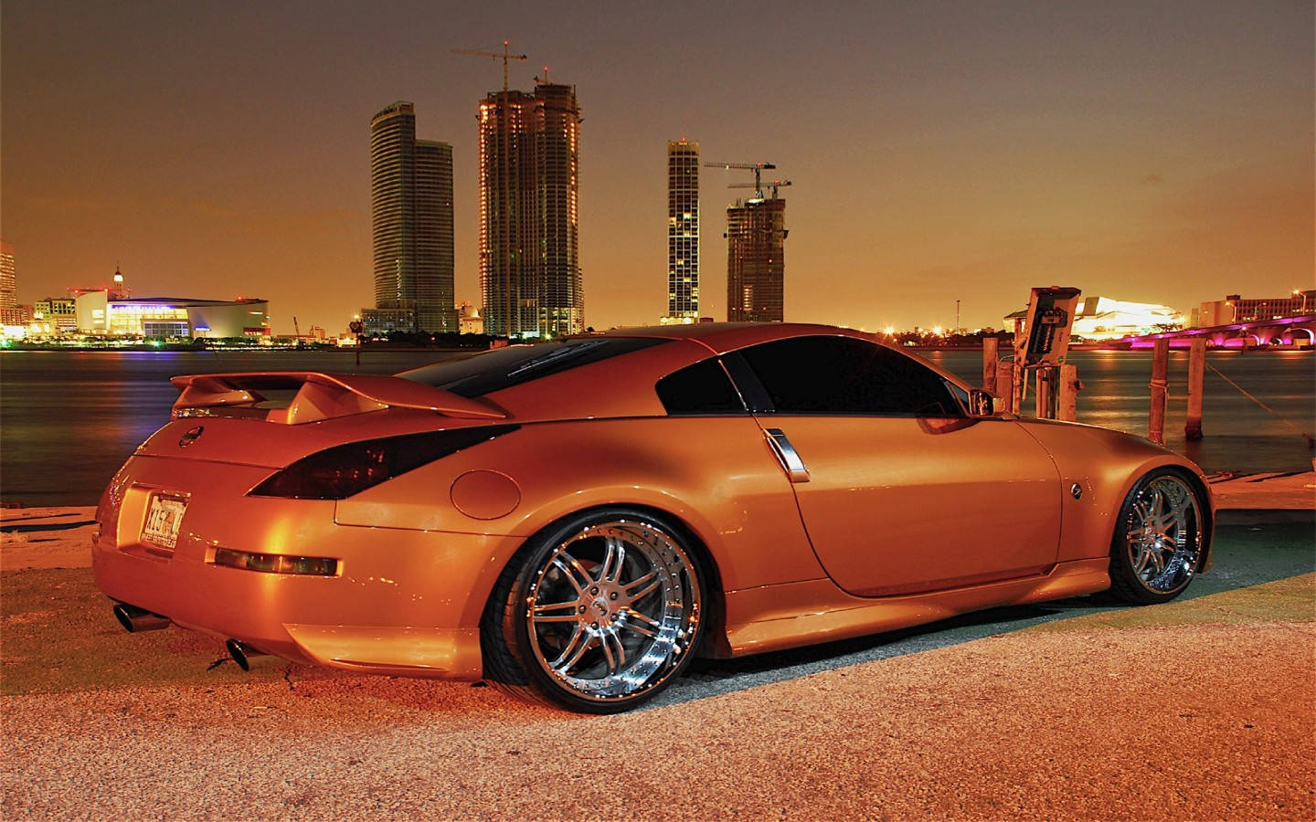 以 Nissan 350Z 升級您的駕馭體驗 壁紙 — 一輛閃亮的青銅色跑車在黃昏時停泊，背後是亮燈的城市摩天大樓。