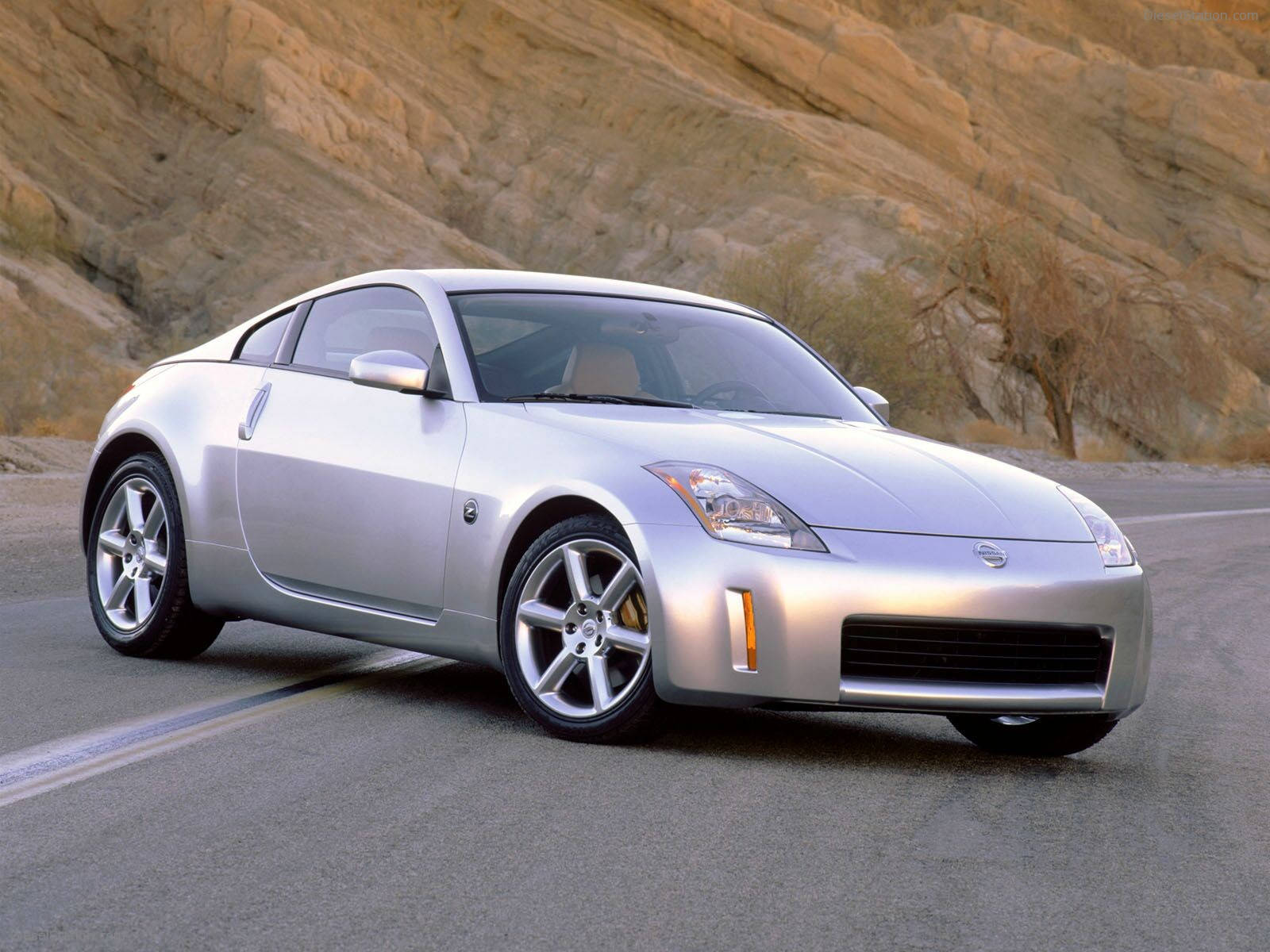 以 Nissan 350Z 的先進設計，展現個人風格 壁紙 — 一架流線型銀色日產350Z跑車在沙漠公路上巡航，背景是崎嶇的岩石地貌。