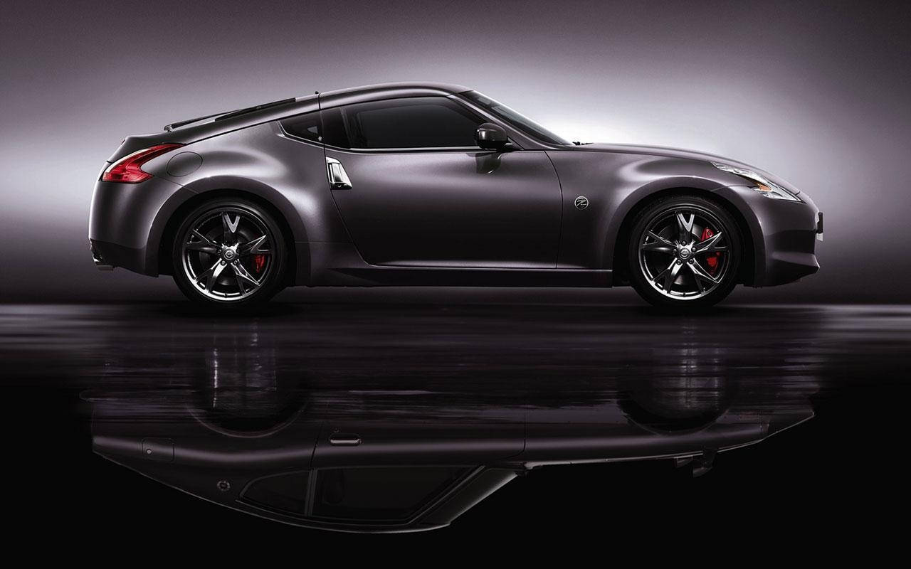 以 Nissan 350z 體驗極致自由 壁紙 — 一輛時尚的啞光灰色跑車配備紅色制動卡鉗，在具有戲劇性燈光和反射地板的攝影棚中展示。