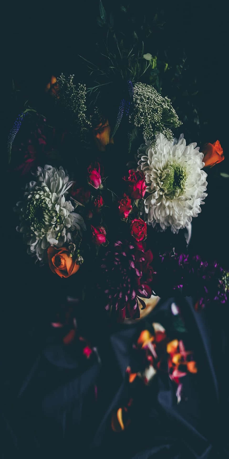 一個陰暗的插花作品，包含紅色、白色和橙色的花朵。