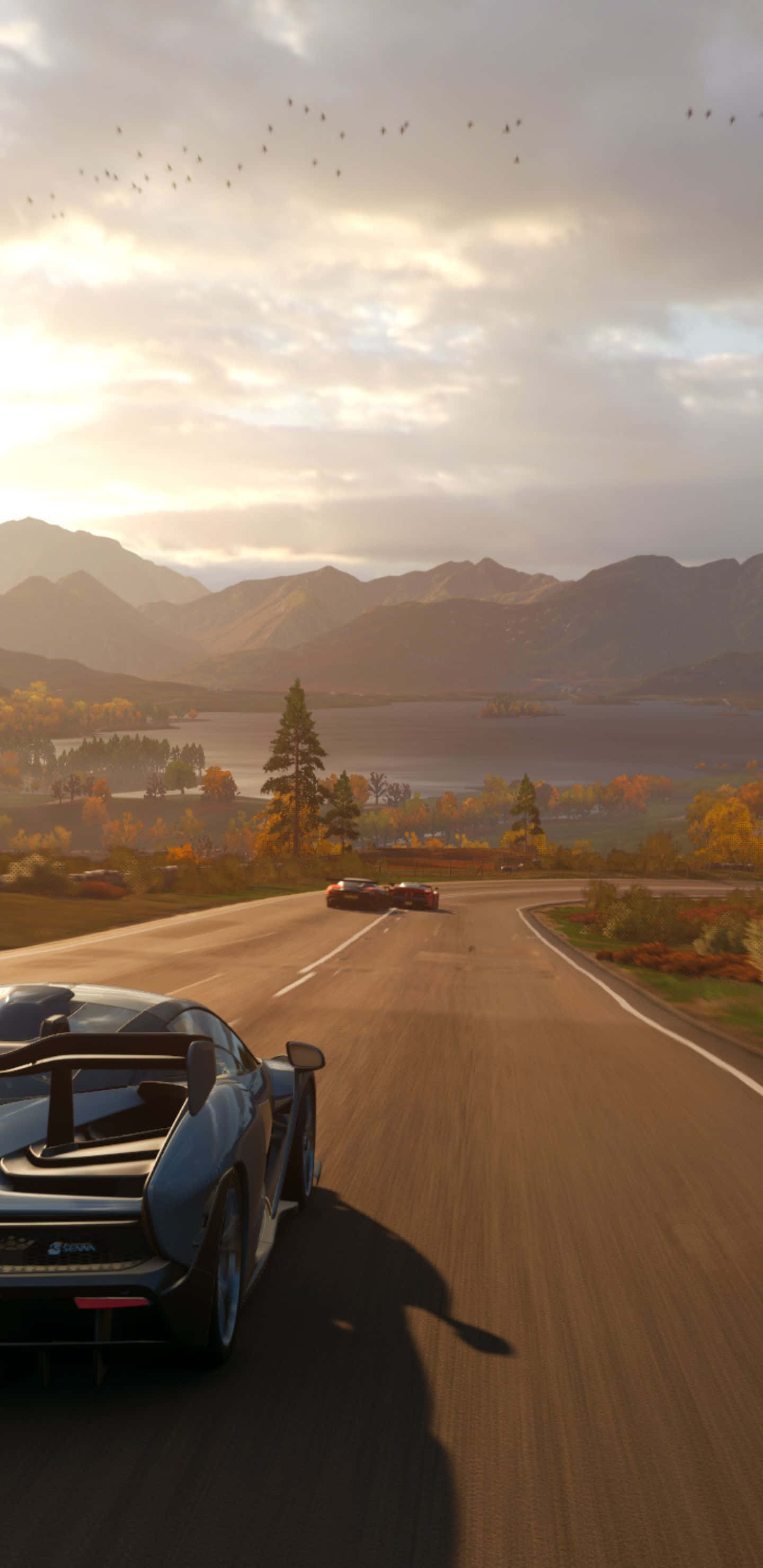 以 Pixel 3XL 和 Forza Horizon 4 解鎖新冒險層次 壁紙 — 一輛時尚的黑色跑車在日落時分沿著蜿蜒的山路飛馳，周圍是秋天的樹木和遠處的山峰，天空多雲。