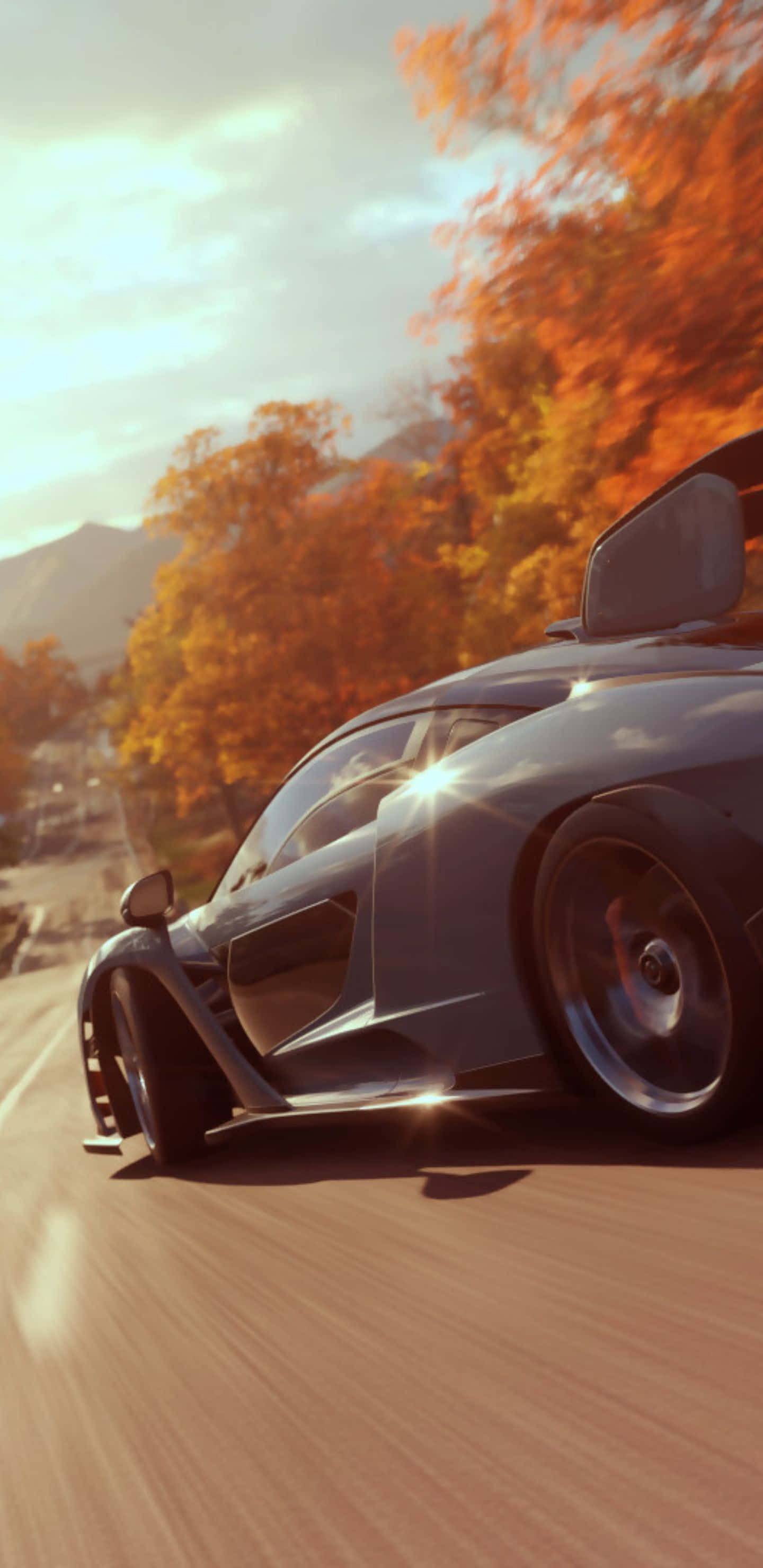 以 Pixel 3XL 在 Forza Horizon 4 中衝向終點線 壁紙 — 一輛時尚的深色跑車在溫暖的金色天空下，沿著兩旁種滿鮮豔橙色秋樹的道路疾馳。