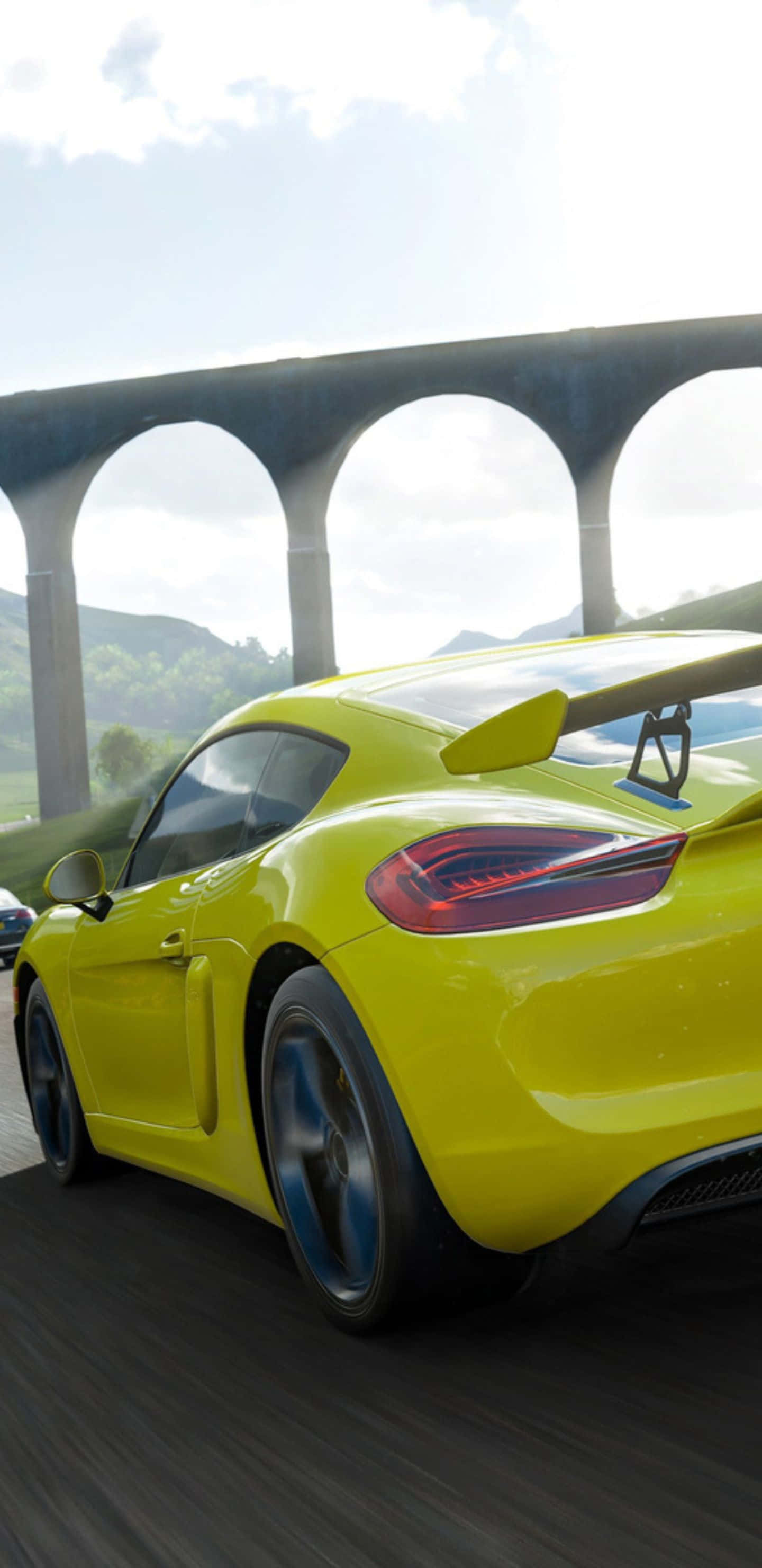 以 Pixel 3XL 探索 Forza Horizon 4 的壯麗開放世界 壁紙 — 一輛充滿活力的黃色跑車在石拱橋下疾馳，運動模糊，背景是朦朧的天空。