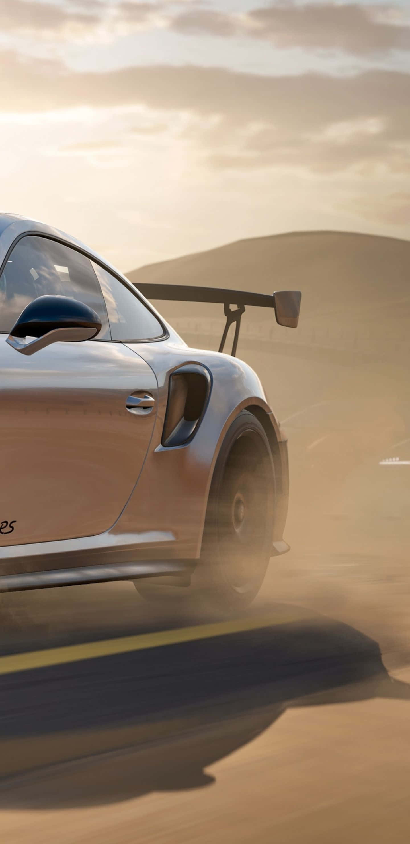 以 Pixel 3XL 與 Forza Motorsport 7 將遊戲體驗提升至巔峰 壁紙 — 一輛銀色跑車帶有大型後擾流板，在金色夕陽天空下的沙漠公路上疾馳，揚起灰塵。