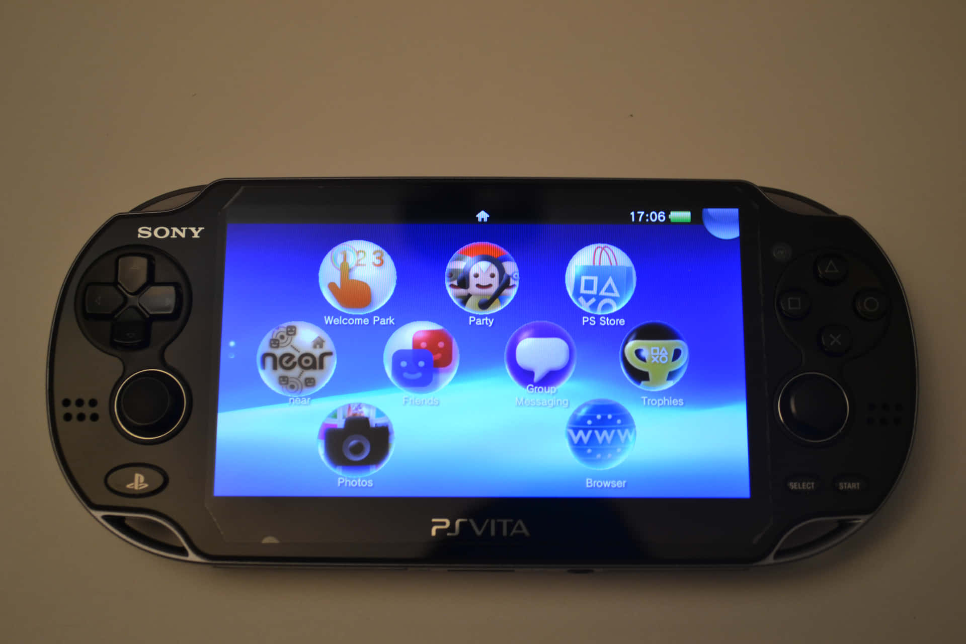以 PlayStation 享受無盡冒險世界 壁紙 — 一部黑色Sony PS Vita手提遊戲機在藍色漸變背景上顯示其主屏幕，帶有色彩繽紛的應用程式圖標。