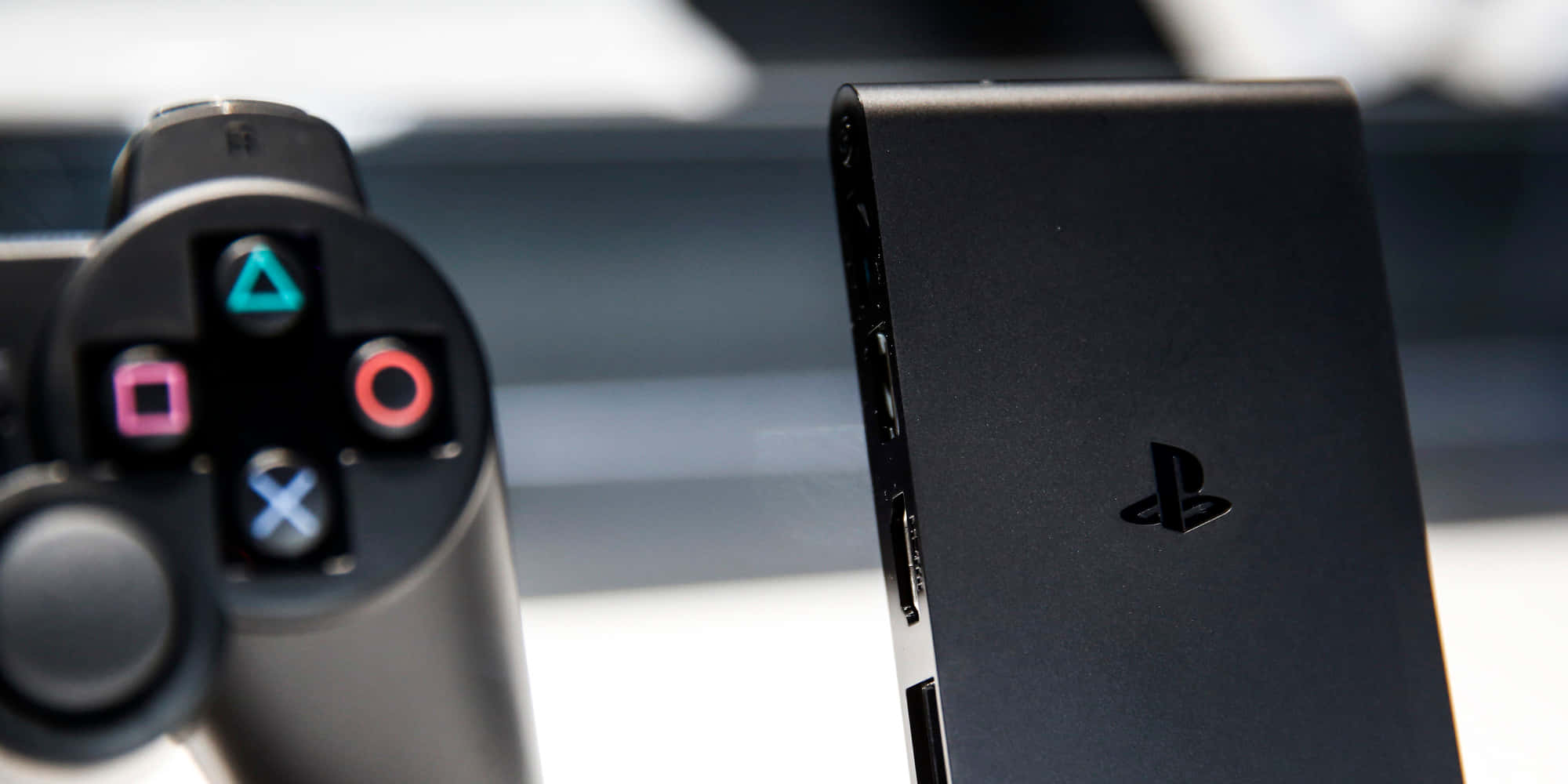 以 PlayStation 探索冒險世界 壁紙 — 黑色PlayStation控制器和主機的特寫，帶有發光的彩色按鈕和時尚的啞光飾面。