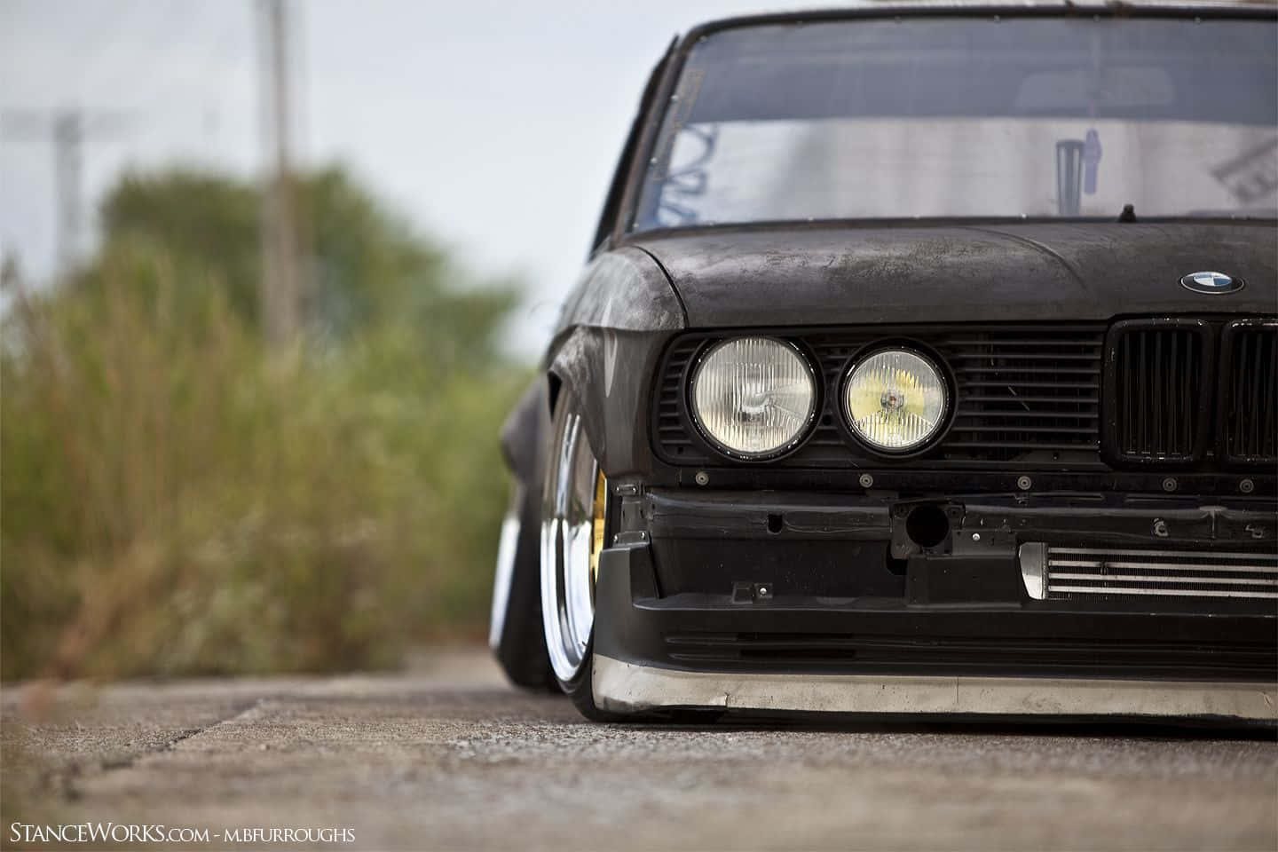 一架改裝的黑色BMW E30，降低懸掛，停在風化的道路上。