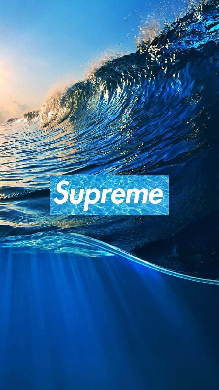 以 Supreme 藍色系列提升你的穿搭品味 壁紙 — 巨大的藍色海浪在頭頂翻捲，陽光在其頂峰閃爍，一個白色的Supreme標誌漂浮在水中。