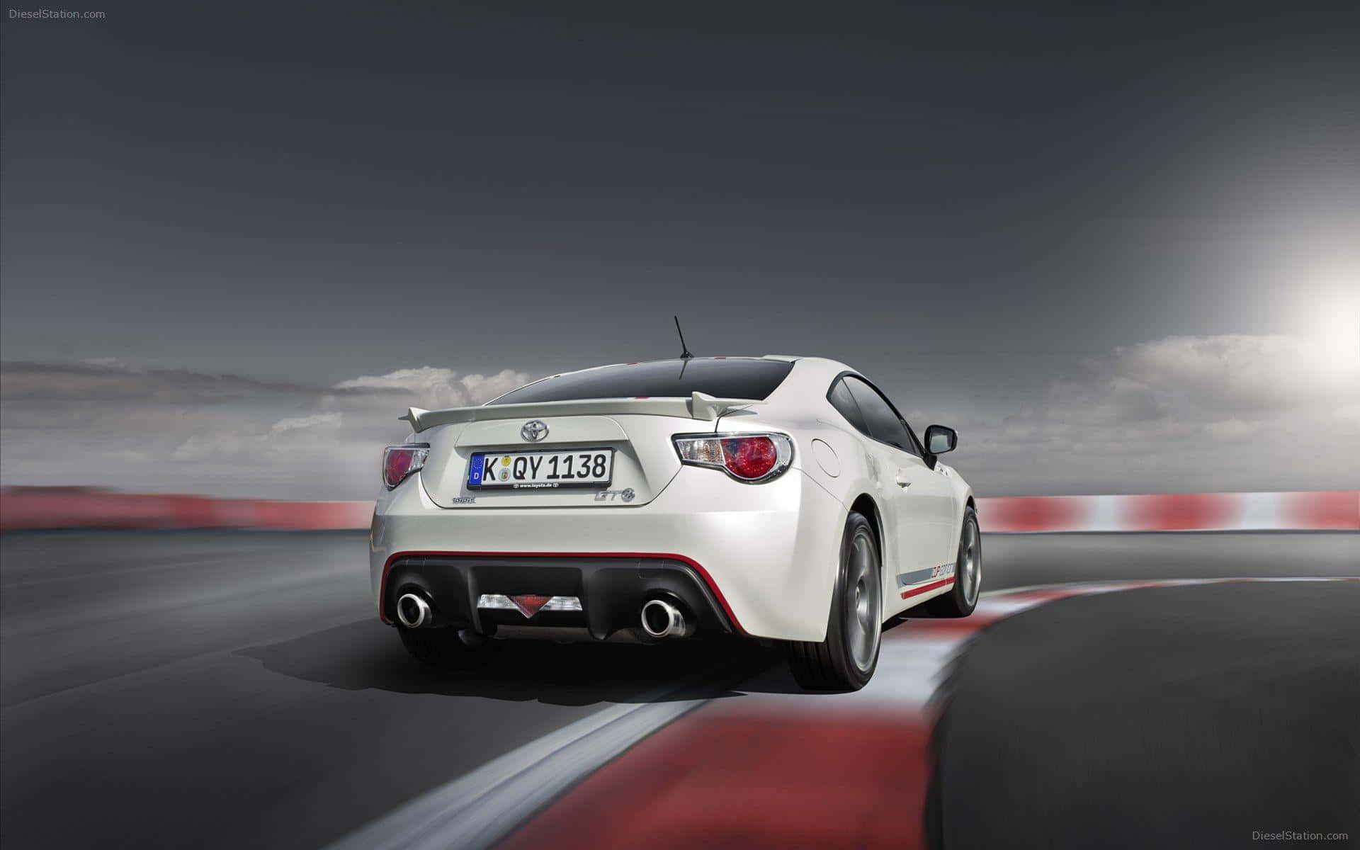以 Toyota 86 將您的駕駛體驗提升至新境界 壁紙 — 一輛白色豐田86跑車在陰天之下，於賽道彎位高速行駛，路緣為紅白色。