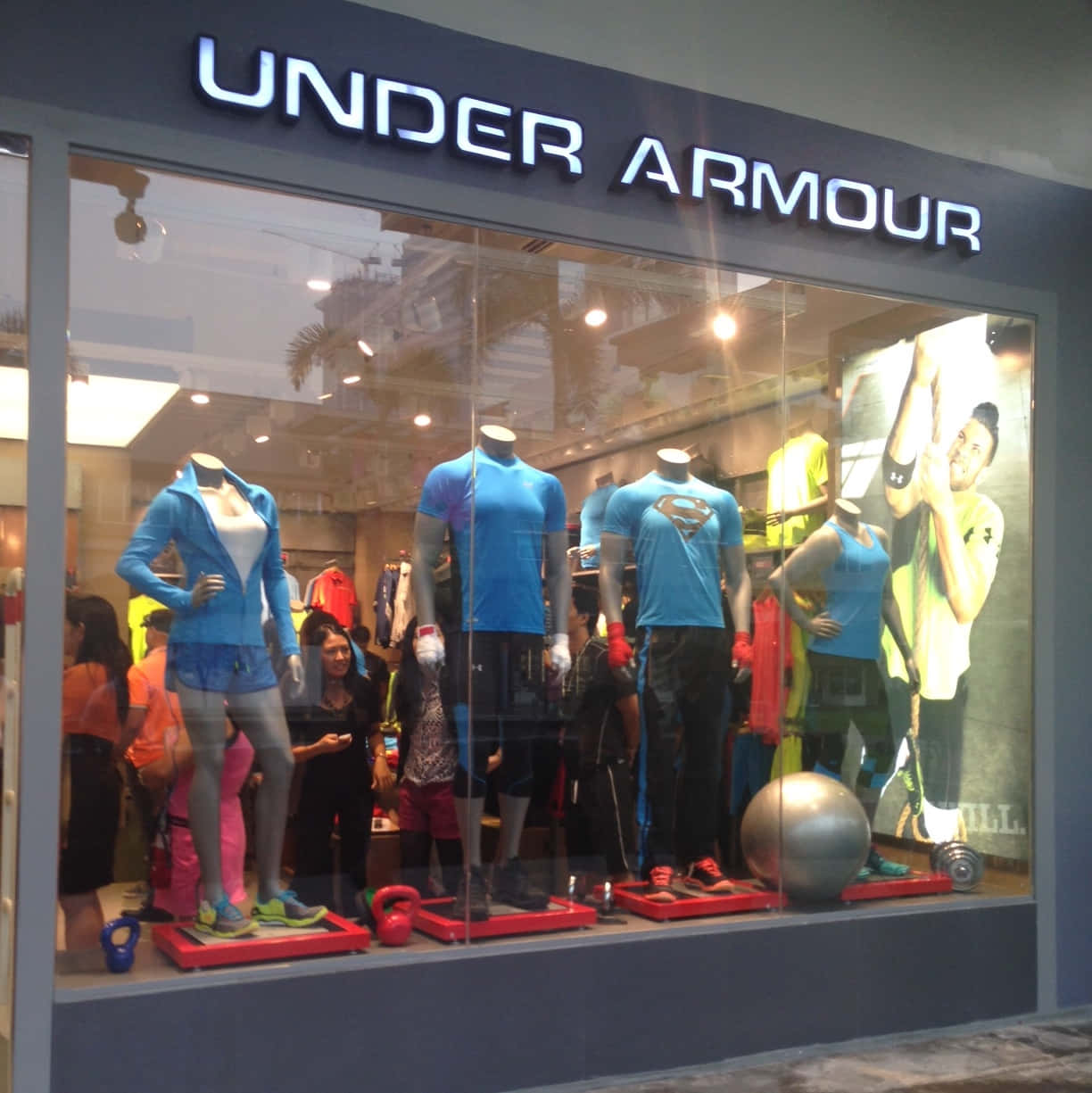 Under Armour 商店櫥窗，模特兒穿著運動服飾，外面有人。