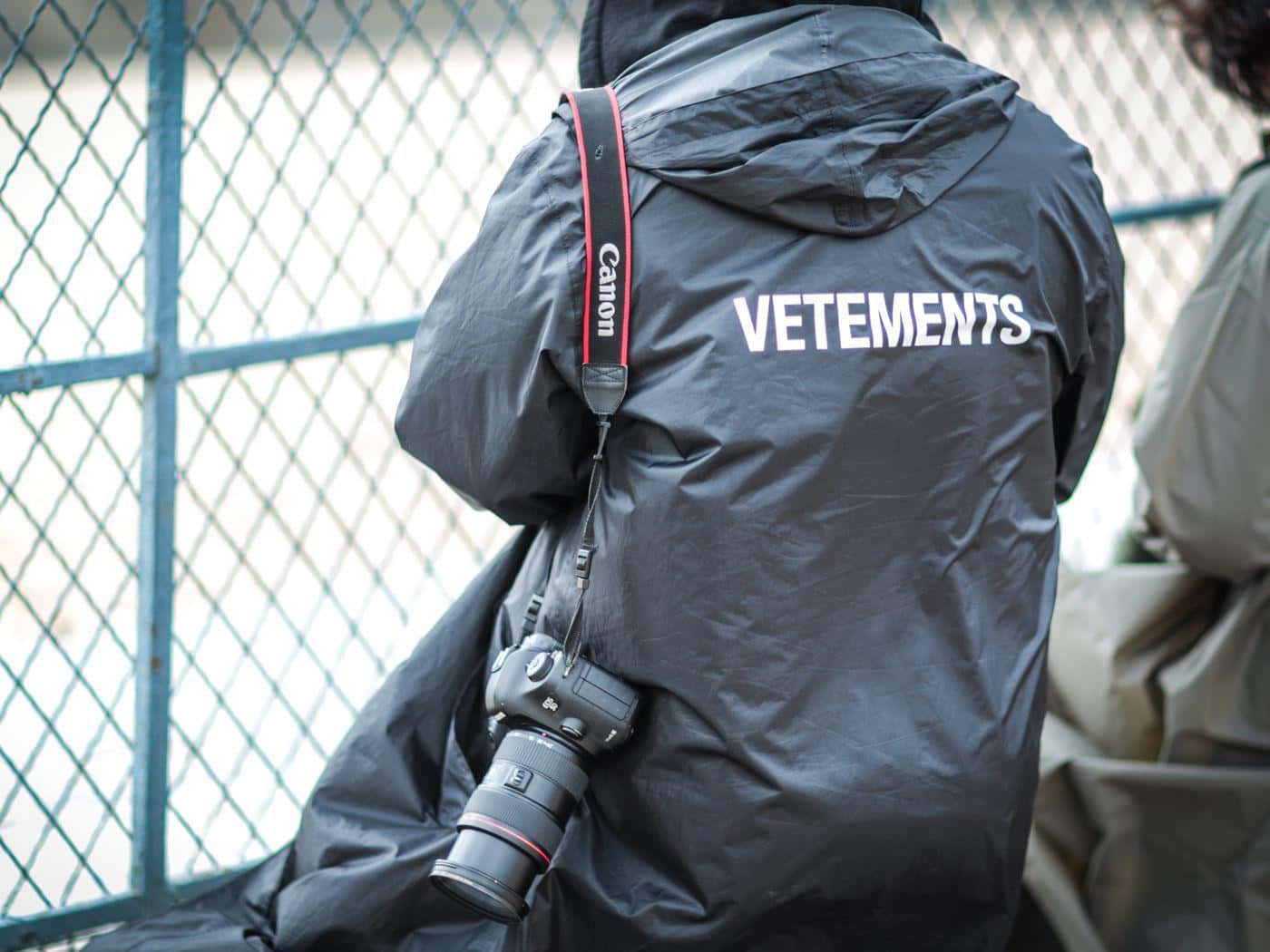穿著黑色Vetements外套的人，肩上掛著Canon相機。
