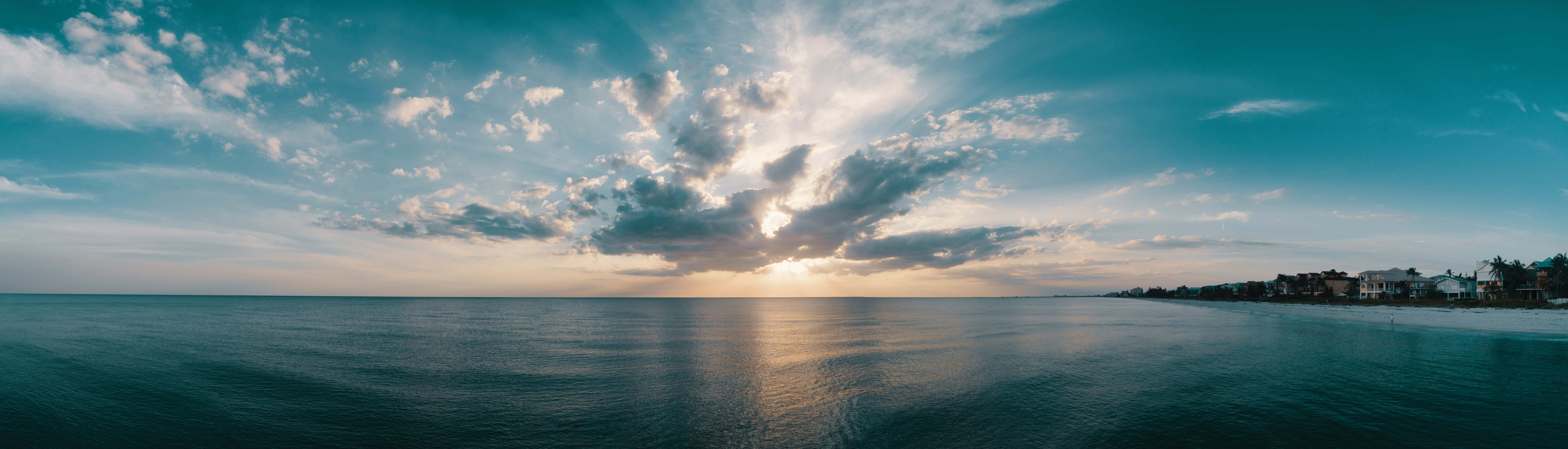 海洋上的日落，有雲和遠處的海灘房屋