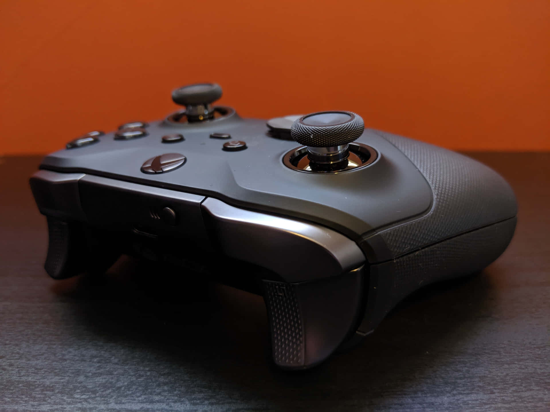 一個黑色Xbox手掣放在木桌上，橙色背景。