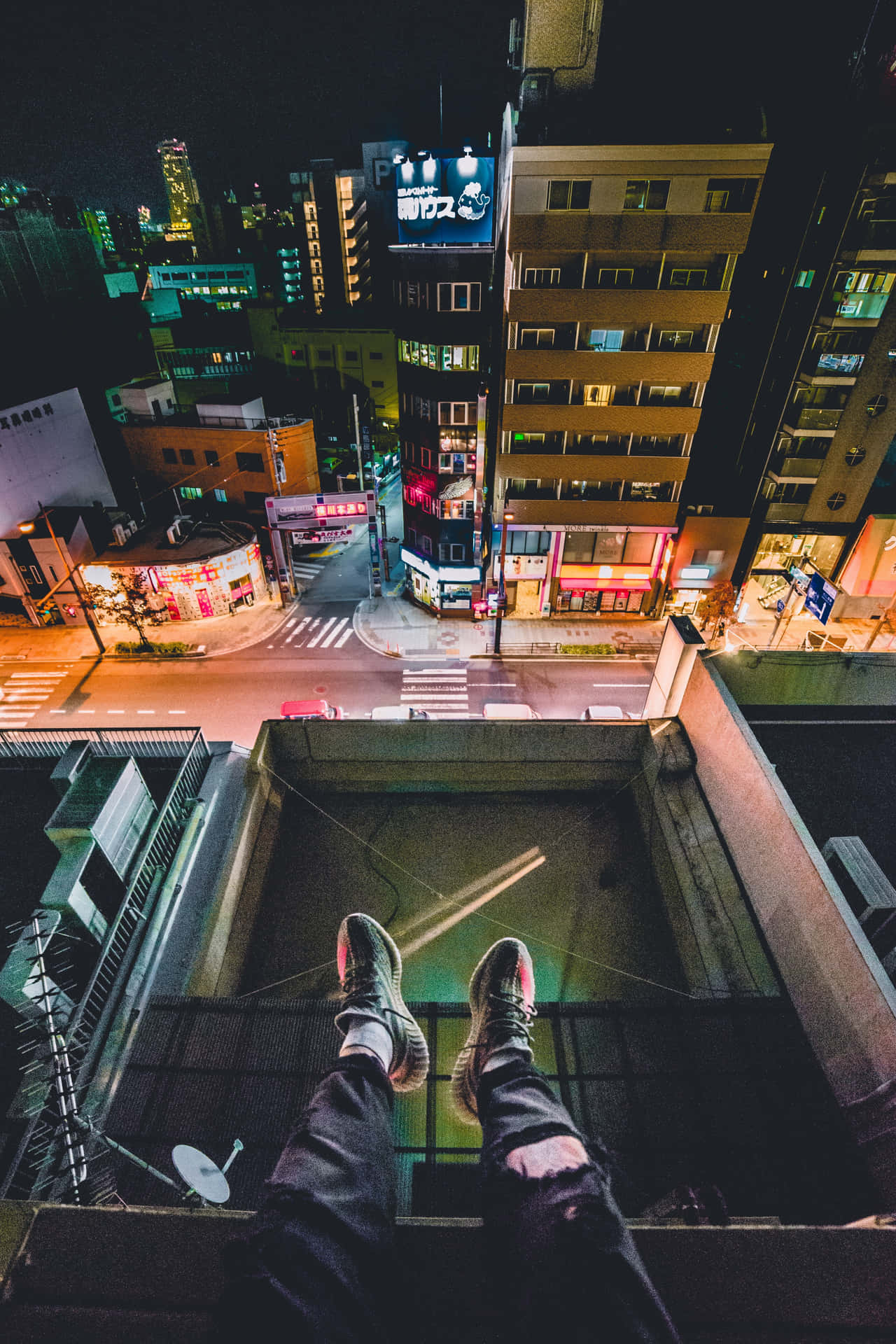 雙腳從屋頂邊緣垂下，懸在夜晚發光的城市街道上方。