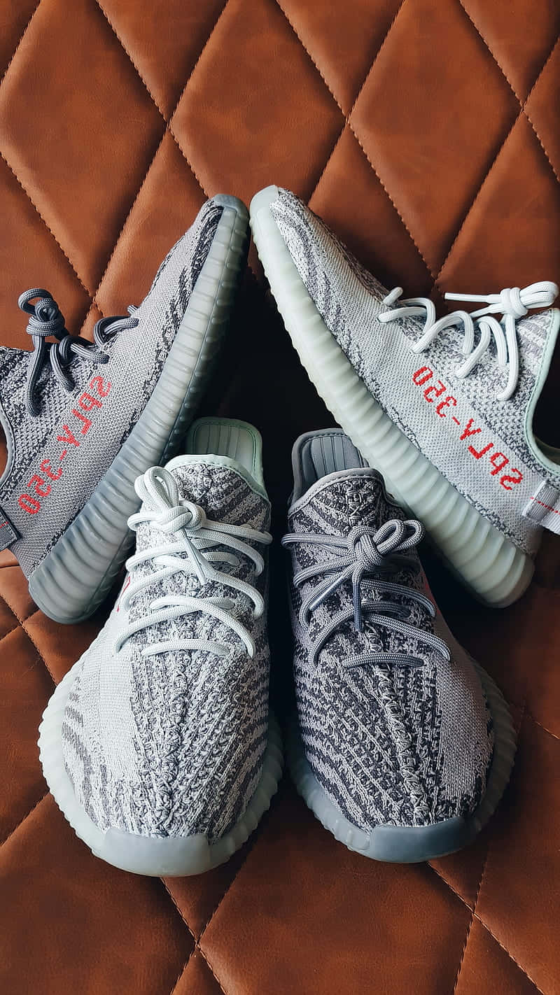 灰色針織Yeezy運動鞋，帶有紅色文字，置於棕色絎縫皮革上。