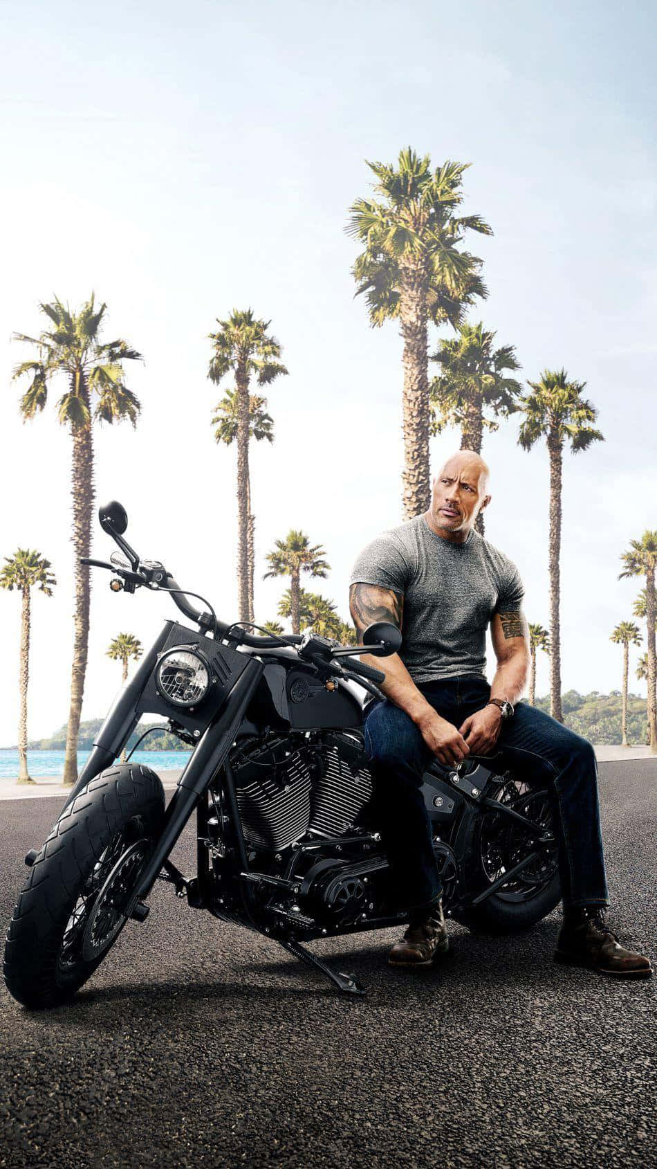 Dwayne Johnson 坐在一輛黑色電單車上，背景有棕櫚樹。