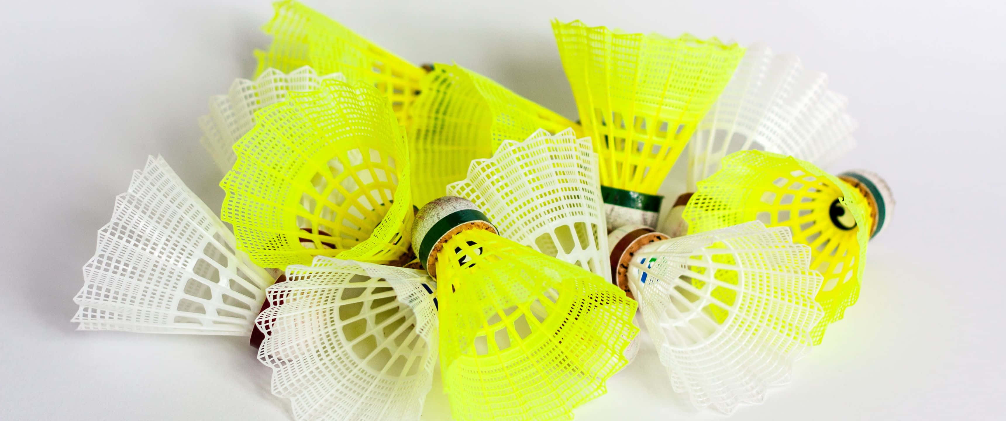以3440x1440p高解析度背景提升羽球實力 壁紙 — 一堆鮮黃色和白色的羽毛球散落在乾淨的白色表面上。