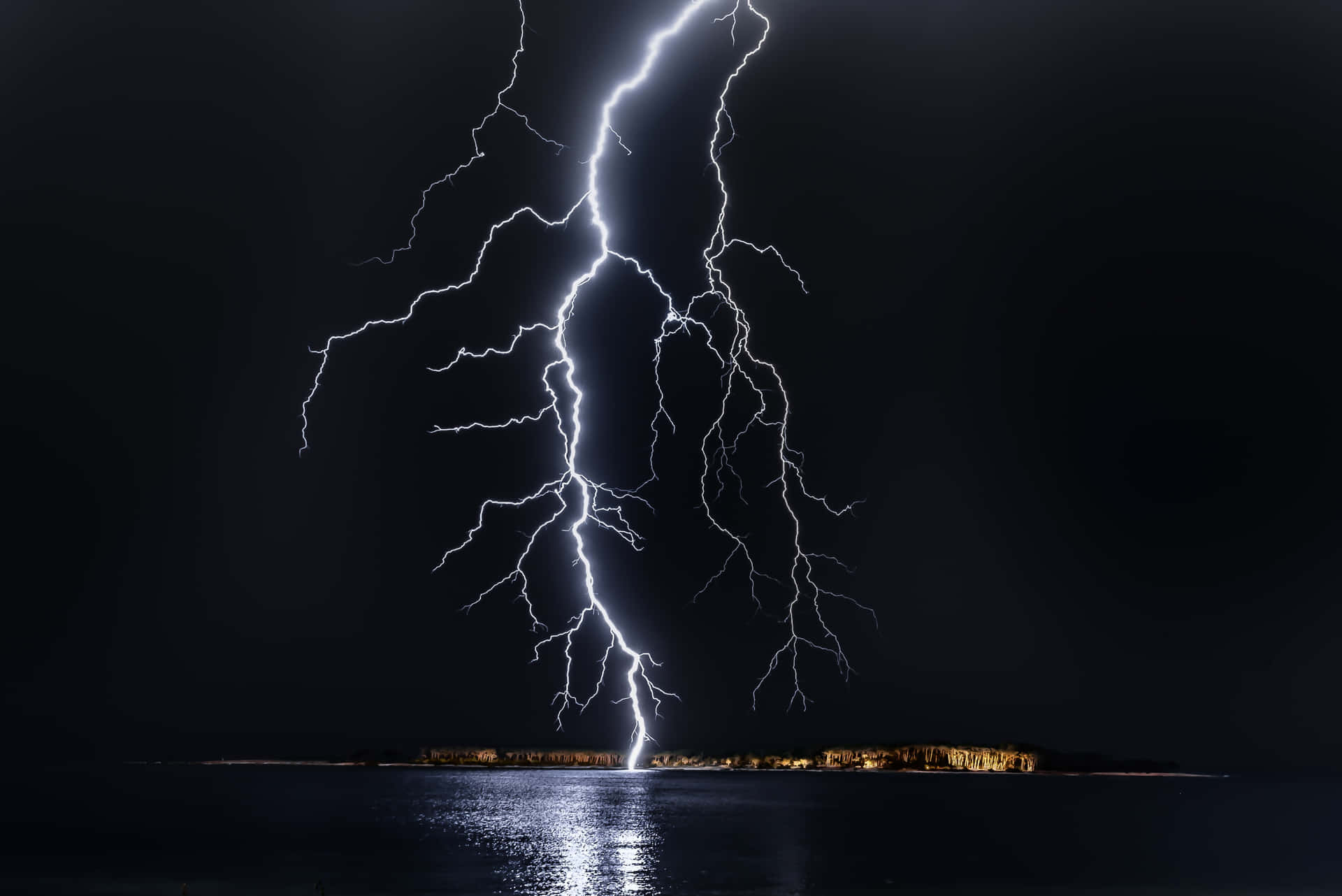 閃電擊中夜間黑暗海岸附近的水面。