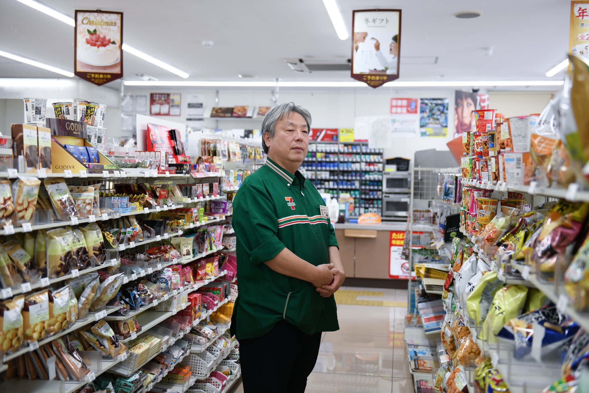 一名店員站在光線充足的便利店通道中，周圍環繞著零食產品。