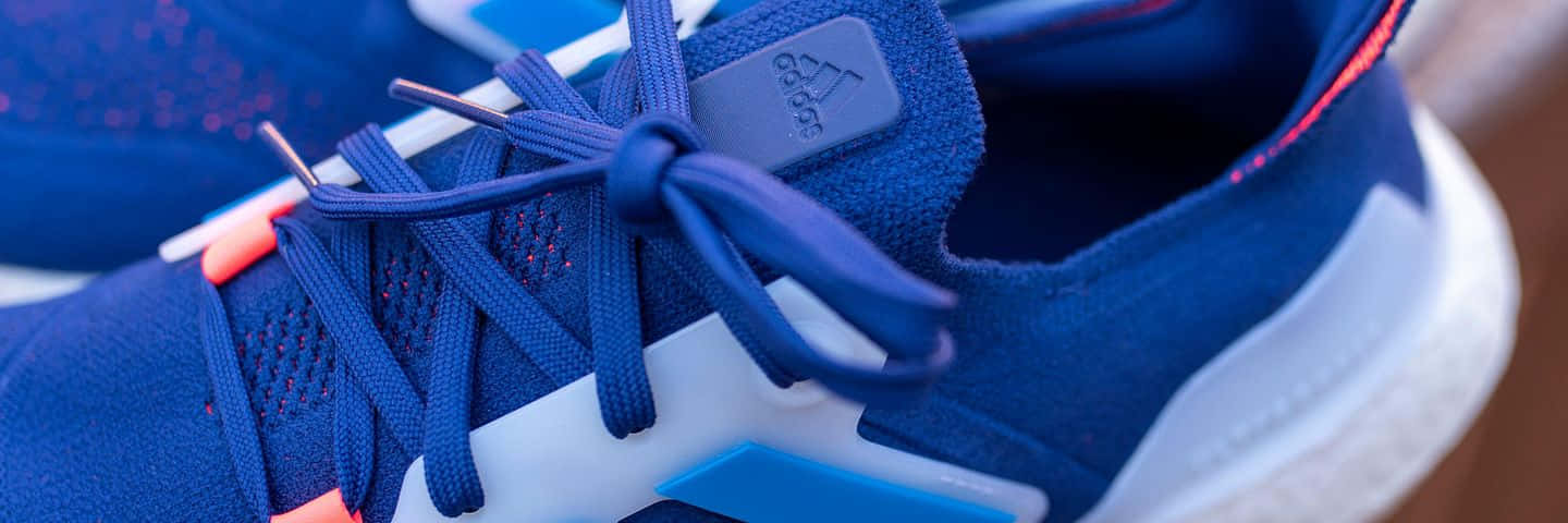 以Adidas提升你的運動表現 壁紙 — 藍色 Adidas 運動鞋特寫，白色鞋底和橙色點綴，展示精細鞋帶和紋理布料。