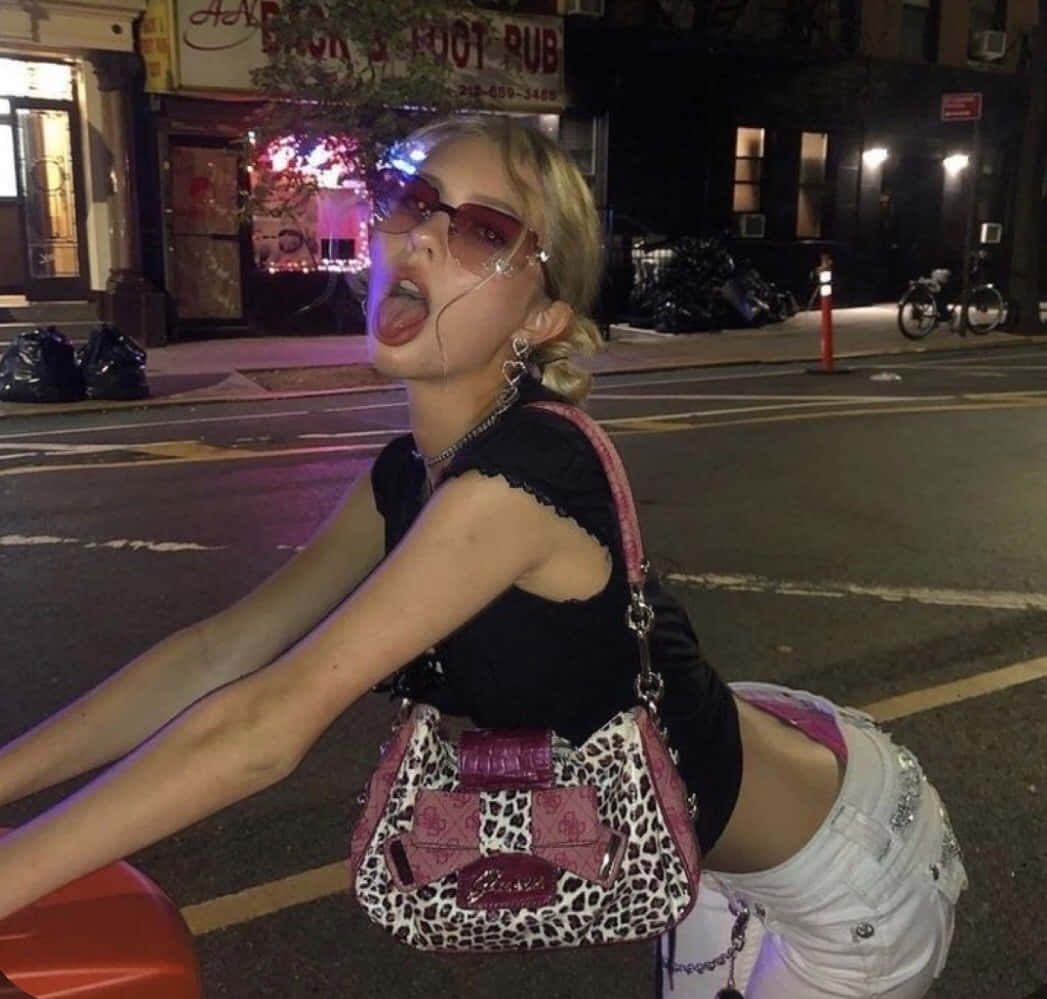 戴太陽眼鏡和豹紋手袋的年輕女子在夜晚城市街道上擺姿勢。 — Baddie 美學 壁紙