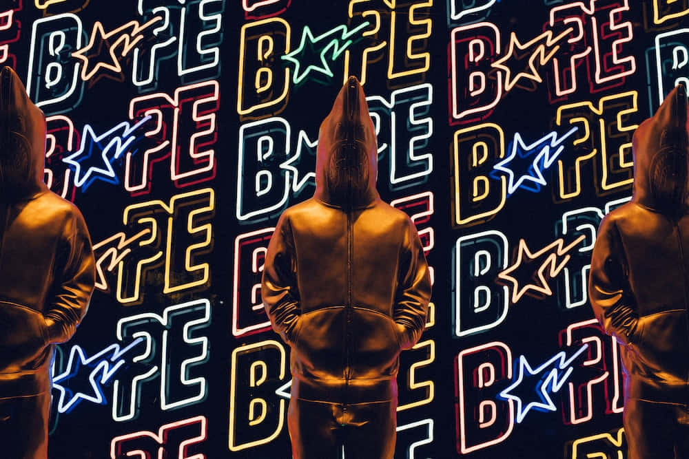 三個戴帽人物面向霓虹燈照亮的Bape標誌牆。