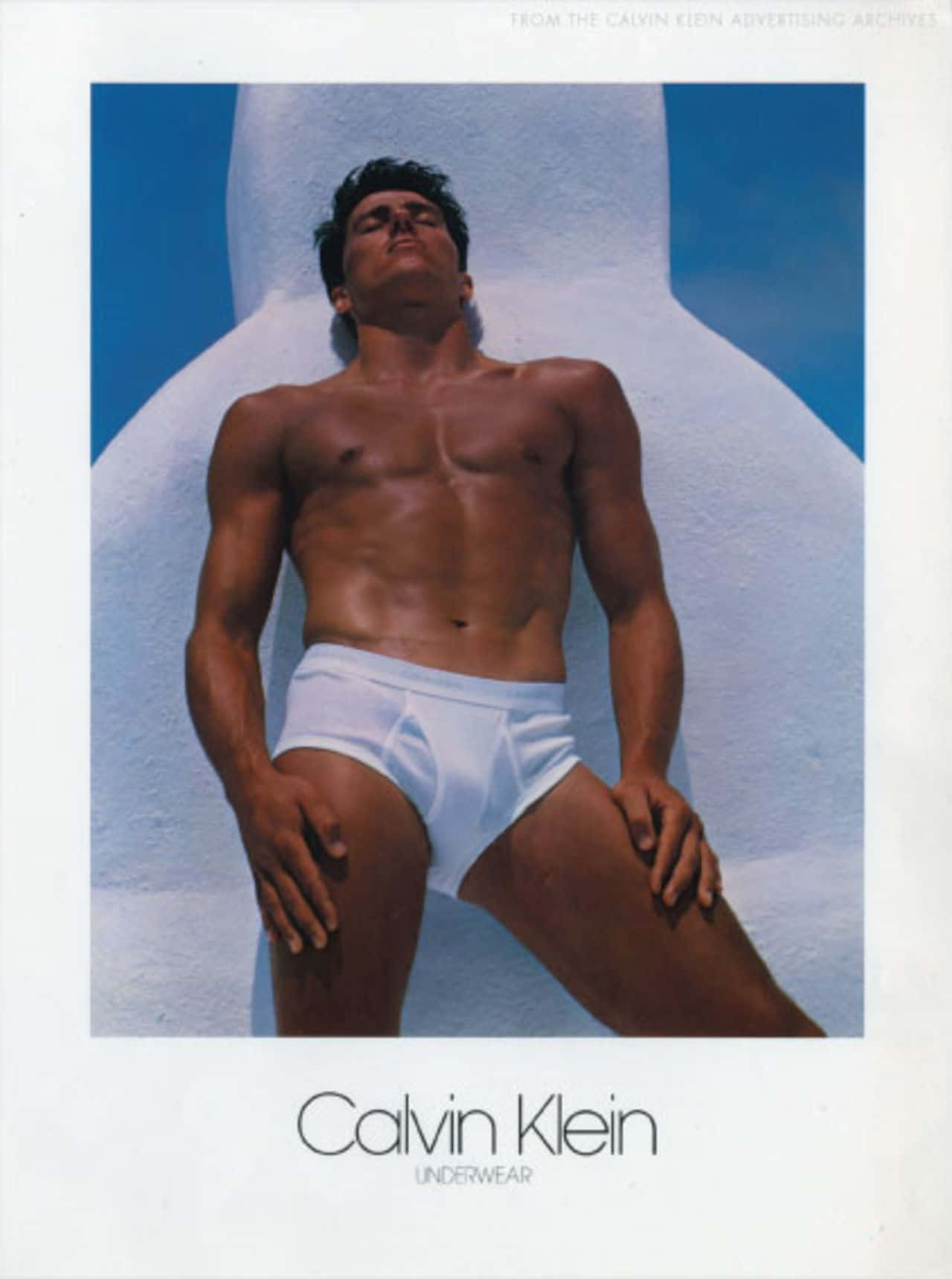 以Calvin Klein展現個人宣言 壁紙 — 一個肌肉發達的男人穿著白色內褲，靠在彎曲的白色牆壁上，背景是明亮的藍天。