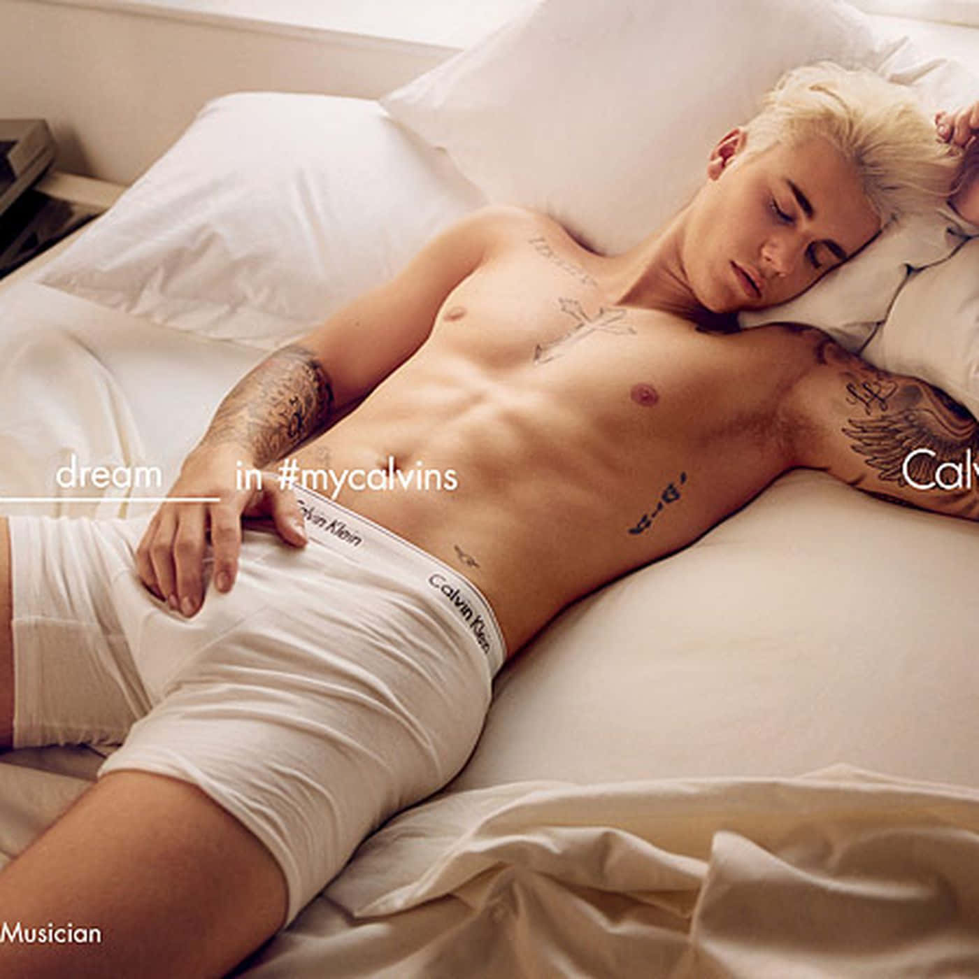 以Calvin Klein展現自信與時尚 壁紙 — 一個冇著衫嘅金髮紋身男人，著住白色Calvin Klein內褲，喺床上安眠。