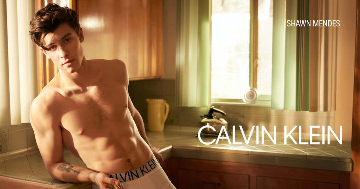 以Calvin Klein展現自信時尚 壁紙 — 一個冇著衫嘅肌肉型男挨喺廚房枱邊，溫暖嘅金色陽光由窗戶射入嚟照住佢。