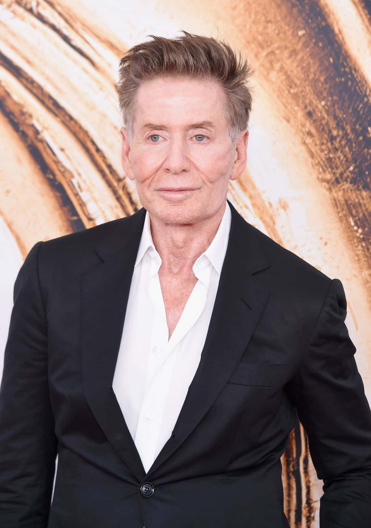 以Calvin Klein從人群中脫穎而出 壁紙 — 一位成熟男士，頭髮經過造型，穿著黑色西裝和白色襯衫，背景是帶有紋理的金色背景。
