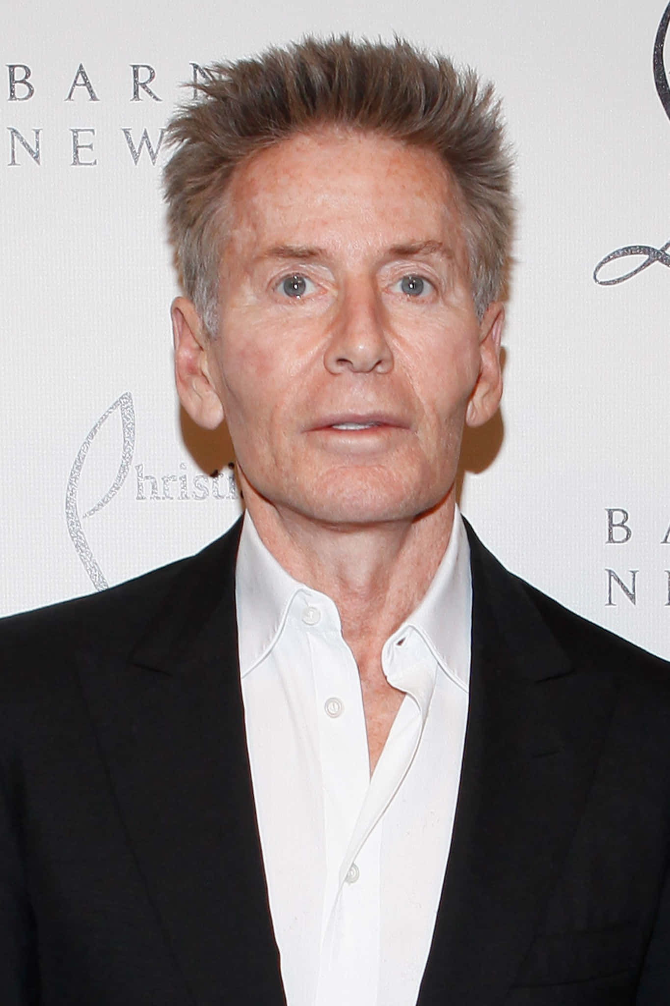 以Calvin Klein製造時尚宣言 壁紙 — 一個有白髮的男人穿著黑色西裝和白色襯衫，在品牌背景前的特寫肖像。