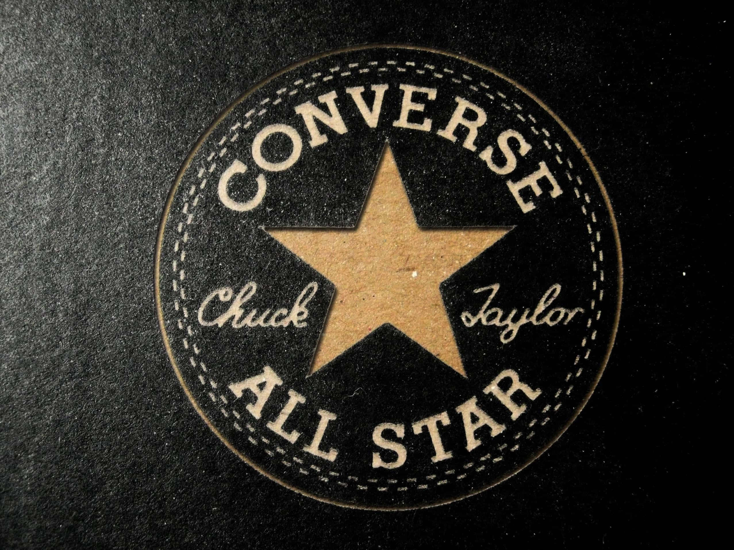 以Converse強化你的風格 壁紙 — 經典 Converse All Star 標誌布章的近距離特寫，在深色紋理布料上帶有米色星星和縫線。
