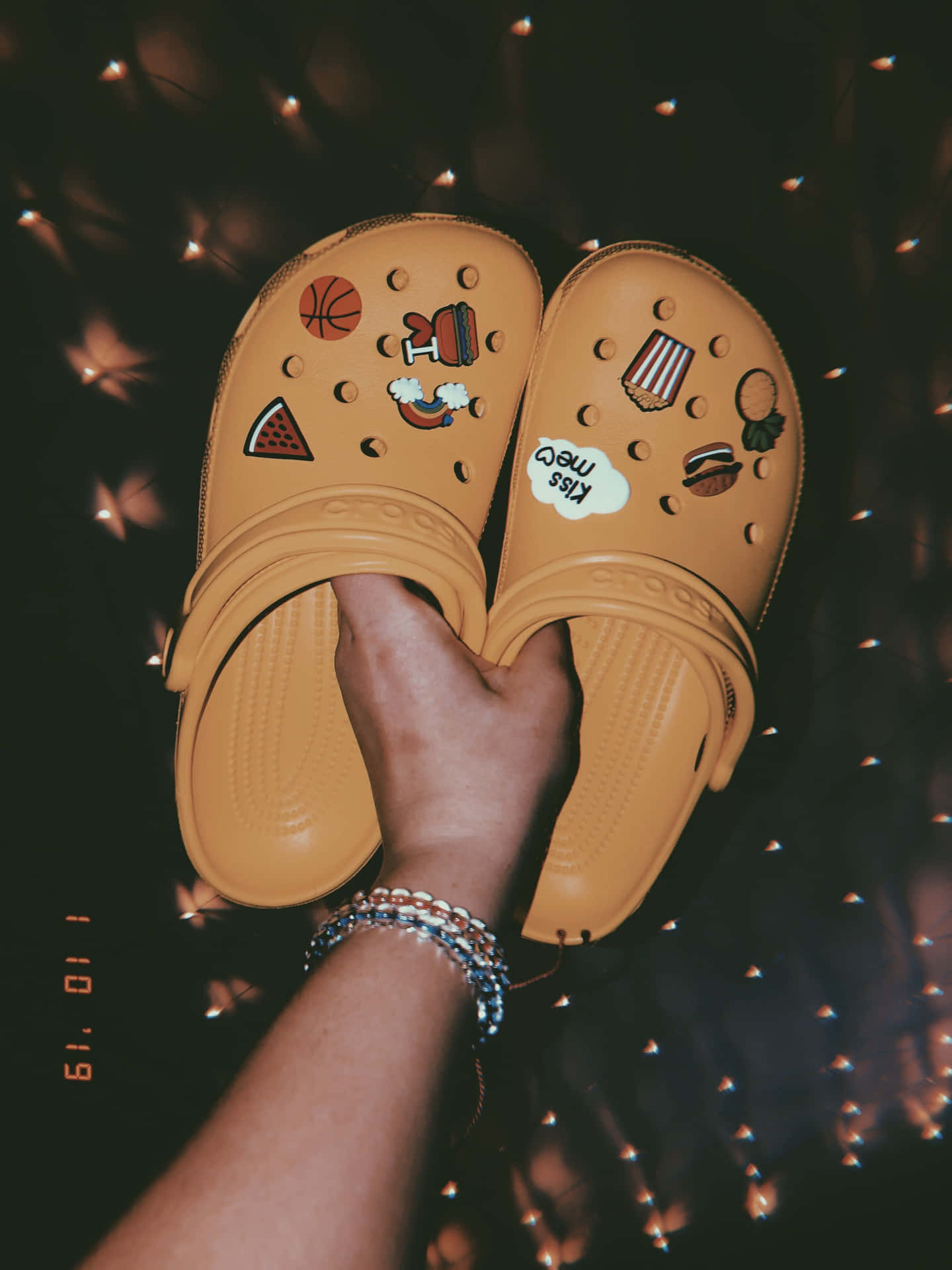 手拿著裝飾有食物和運動貼片的米色Crocs，在仙女燈下。