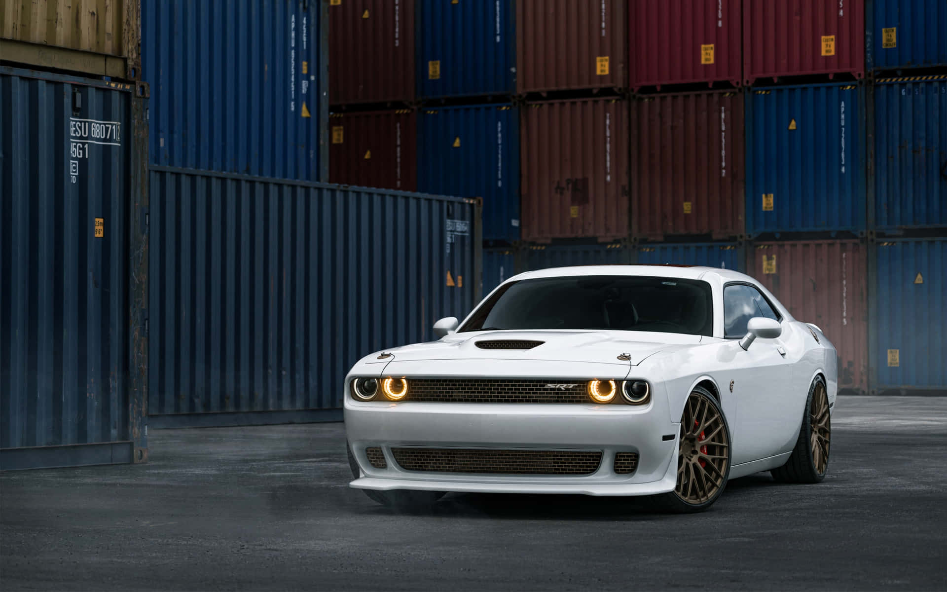 白色 Dodge Challenger RT 夜間停放在堆疊的貨運集裝箱前。