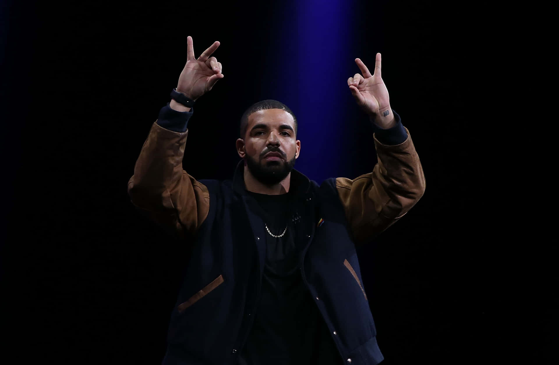 Drake 在藍光下於舞台上做出和平手勢。
