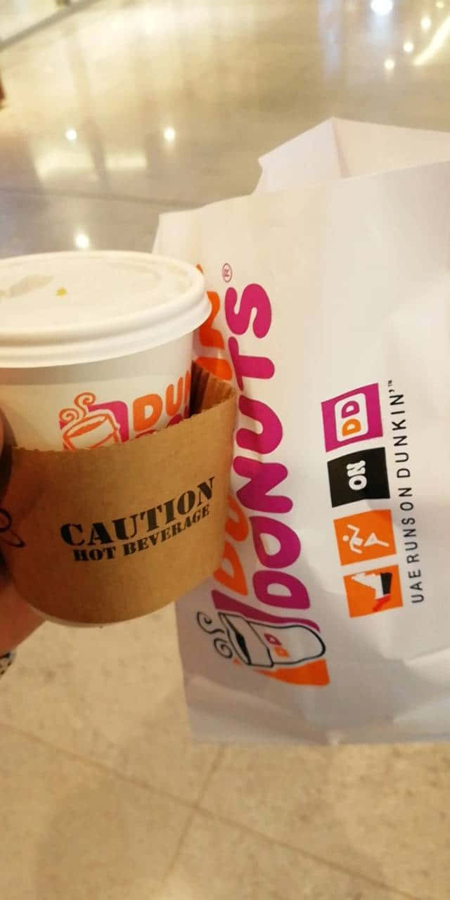 手在瓷磚地板上拿著Dunkin' Donuts咖啡杯和袋子。