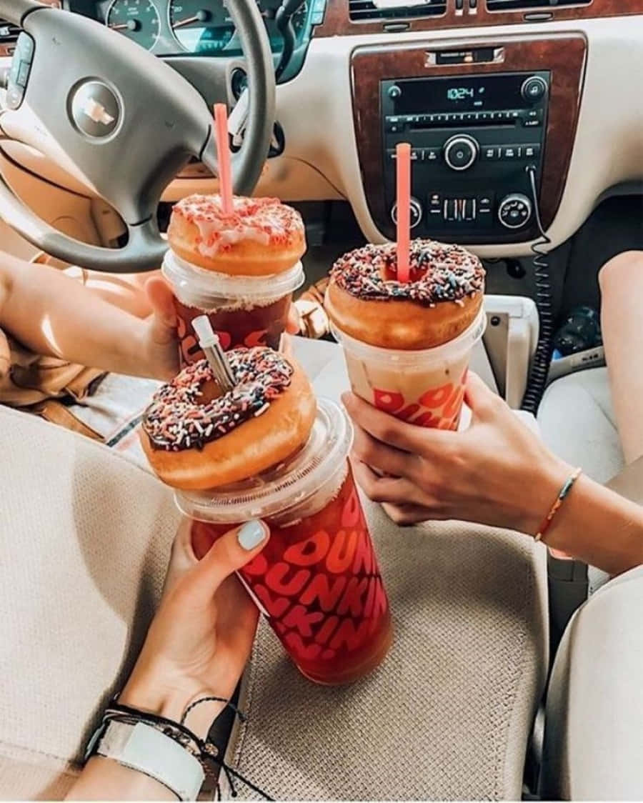 以Dunkin' Donuts美味點心開啓美好早晨！ 壁紙 — 三隻手喺米色內飾同木紋飾邊嘅車入面，拎住上面有冬甩嘅Dunkin' Donuts飲品。