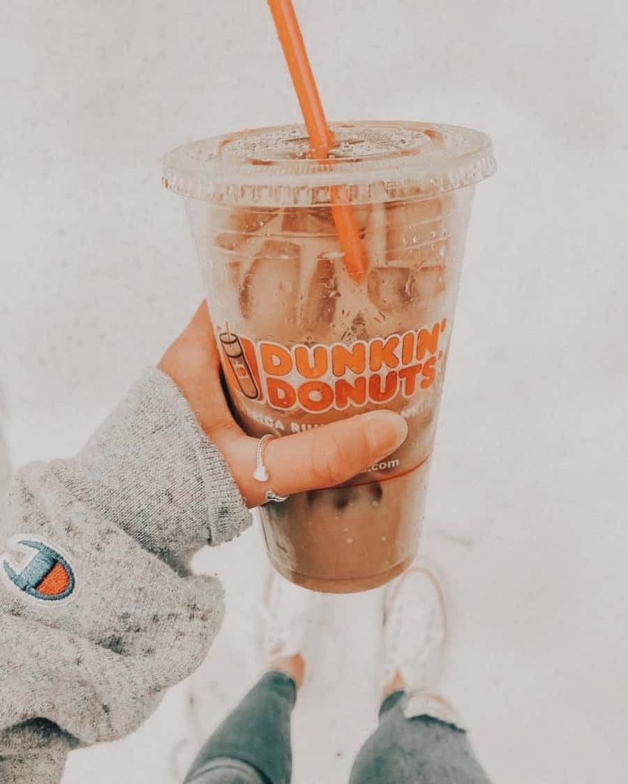 以Dunkin' Donuts開啓美好一天 壁紙 — 一隻穿著灰色衛衣的手，在雪景背景下拿著一杯帶有橙色吸管的Dunkin' Donuts冰咖啡。