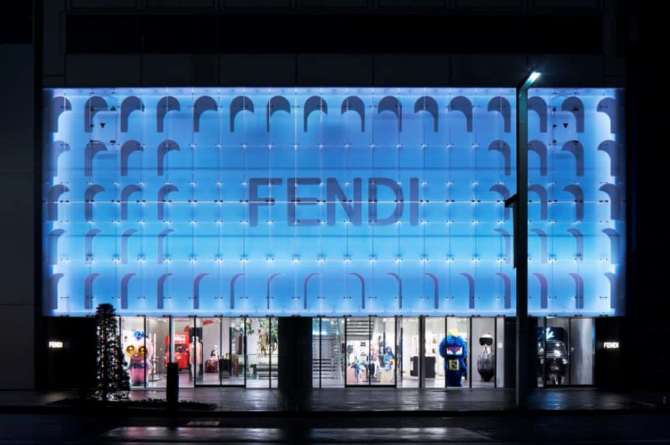 以Fendi繽紛春季系列製造時尚宣言 壁紙 — FENDI 商店外牆在夜間被發光的藍色燈光和重複的拱形圖案照亮。