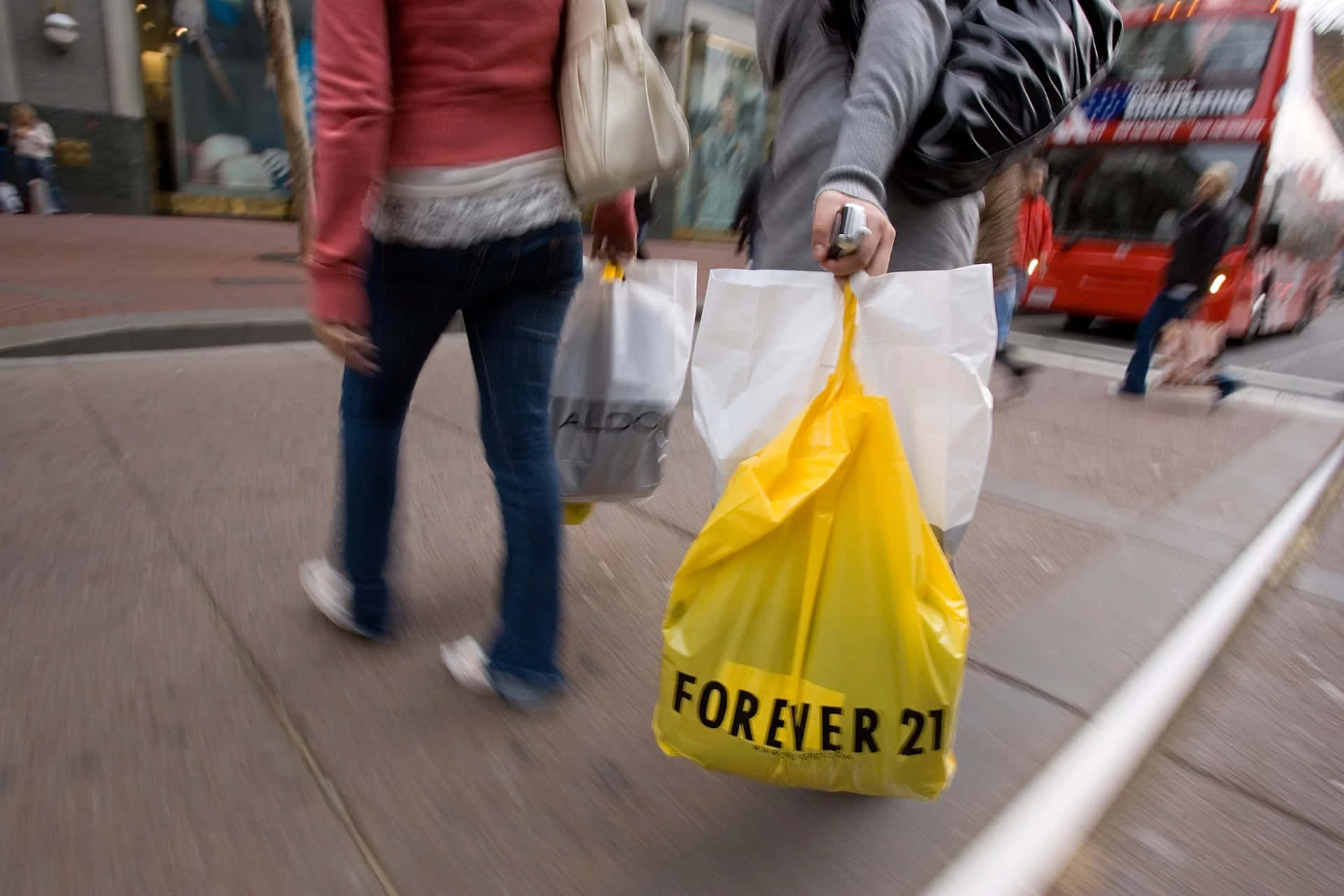 行人手持購物袋（包括一個黃色Forever 21袋）在城市行人道上行走。