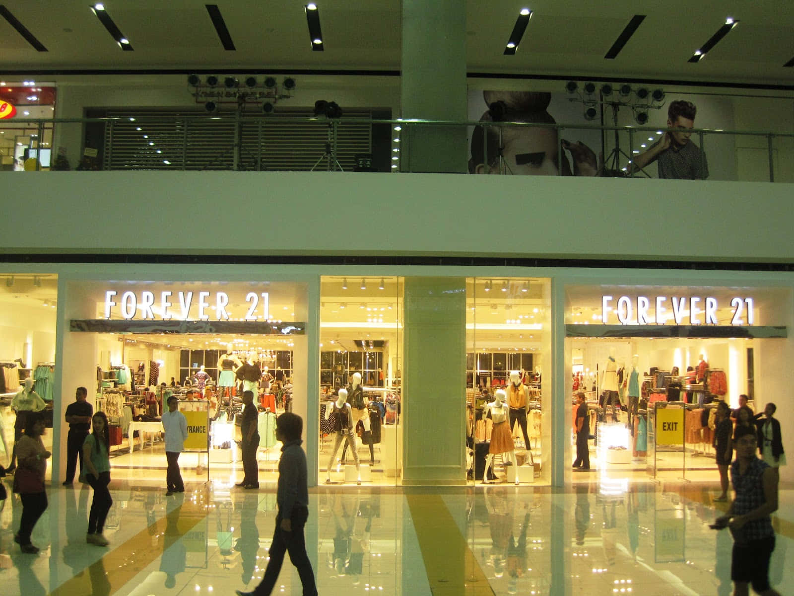 以Forever 21時尚系列迎接新季，煥然一新 壁紙 — 購物者走過光線明亮的Forever 21商店，位於一個繁忙的兩層購物中心，地板反射光線，頭頂有燈光。