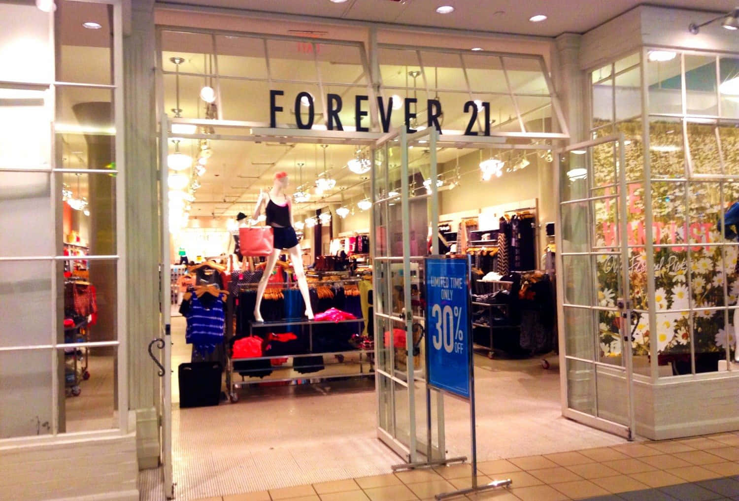 以Forever 21時尚風格成為時尚偶像 壁紙 — 光線明亮的Forever 21商店入口，玻璃門敞開，展示人體模型、貨架和30%折扣標誌。