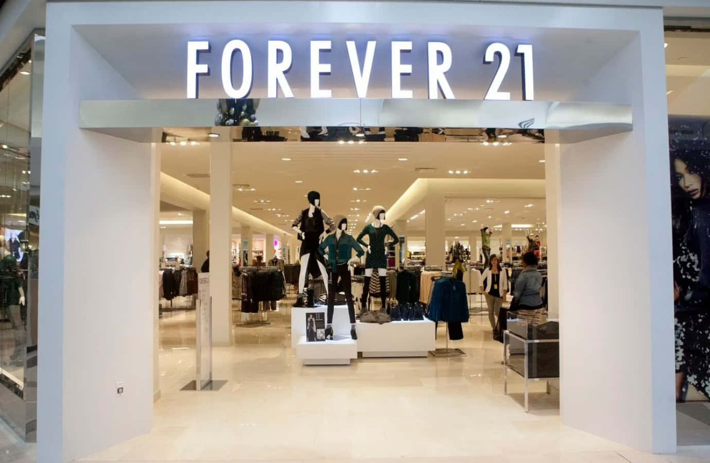 以Forever 21的最新潮流更新你的衣櫥 壁紙 — 光線明亮的Forever 21商店入口，模特兒穿著時尚服裝在發光招牌下展示。