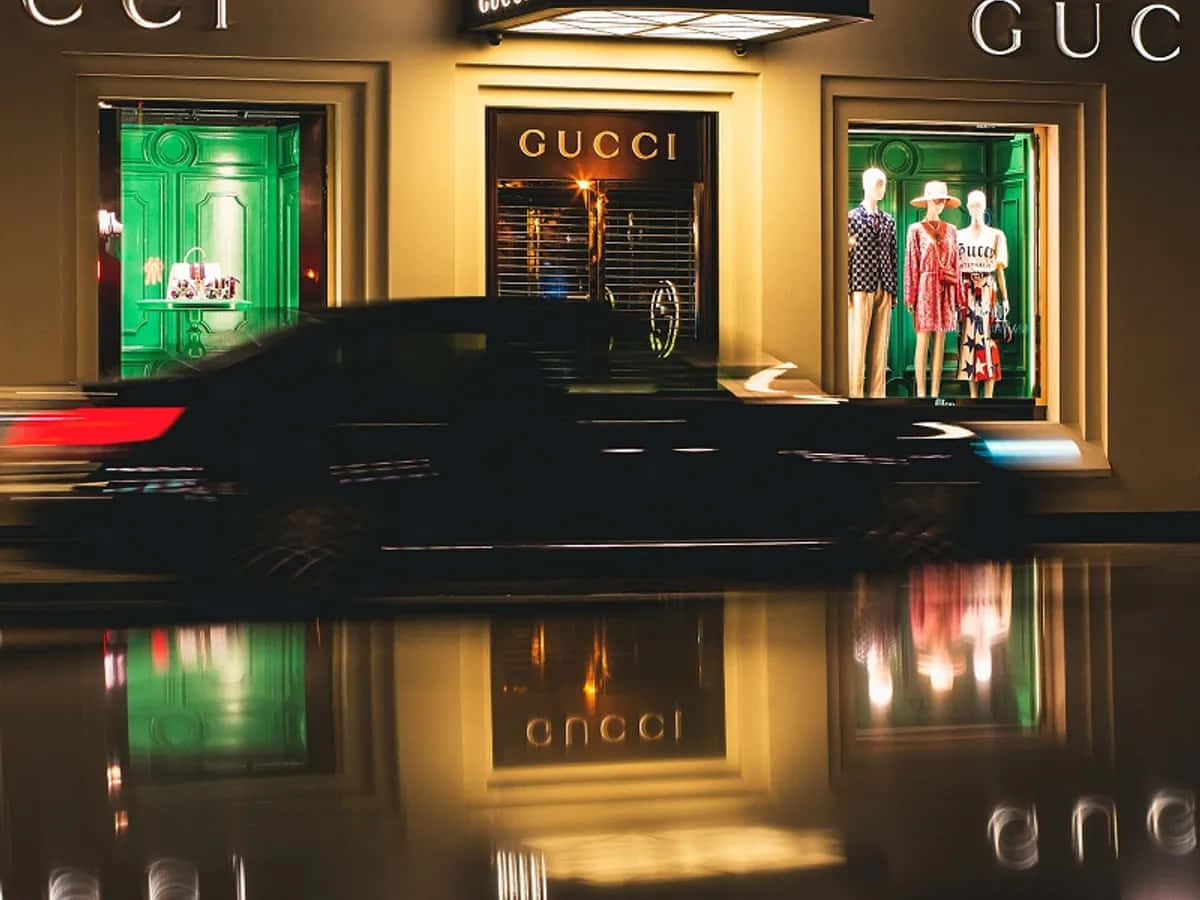 黑色汽車在夜間駛過Gucci商店，霓虹綠色窗戶和金色招牌映照在濕漉漉的人行道上。