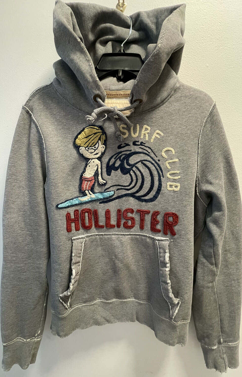 灰色破舊Hollister連帽衛衣，衝浪圖案掛在衣架上。