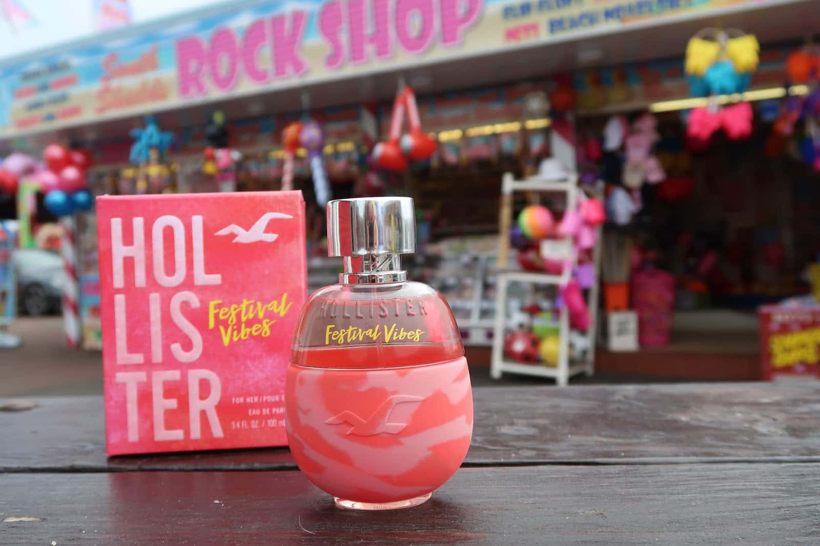 粉紅色Hollister香水瓶和盒子放在色彩繽紛商店外的木桌上。