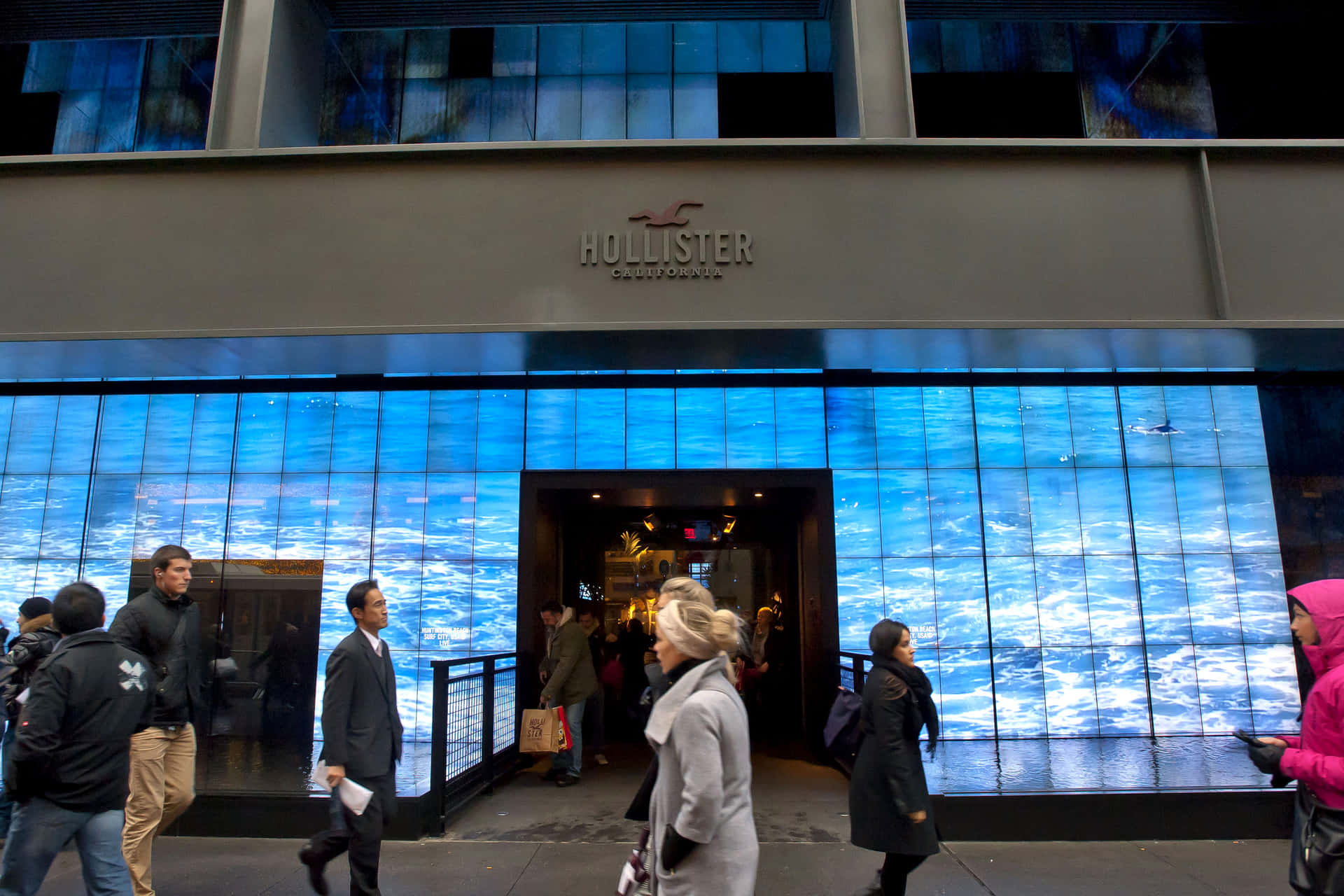 人們夜晚經過一間設有藍色海浪數碼顯示屏的Hollister商店。