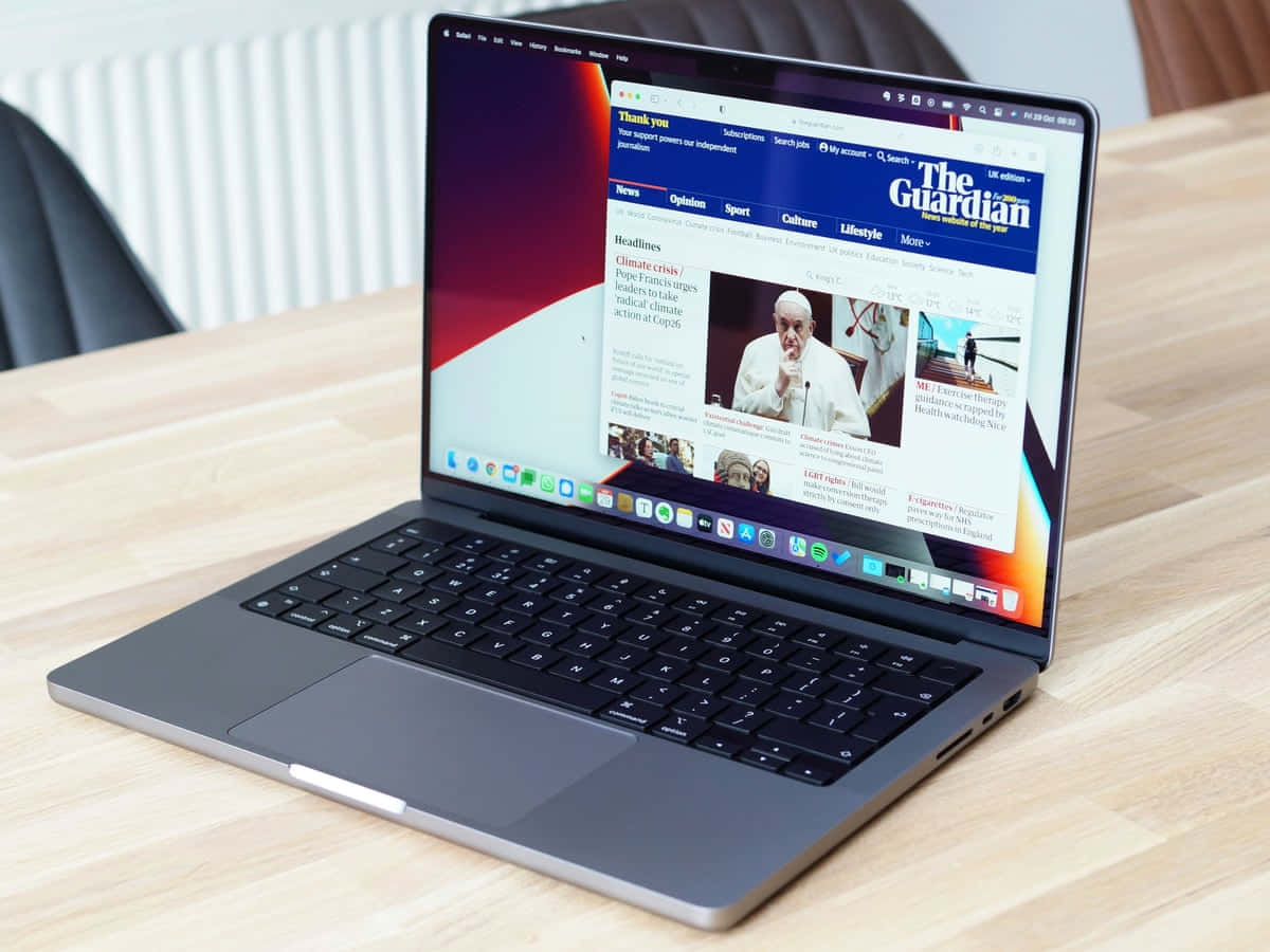 以MacBook輕鬆應對任何任務 壁紙 — 一部時尚的銀色手提電腦在現代室內環境中的木桌上顯示The Guardian新聞網站。