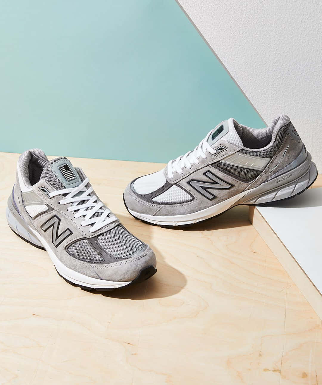 灰色New Balance運動鞋放在木質表面上，背景為藍綠色和白色。